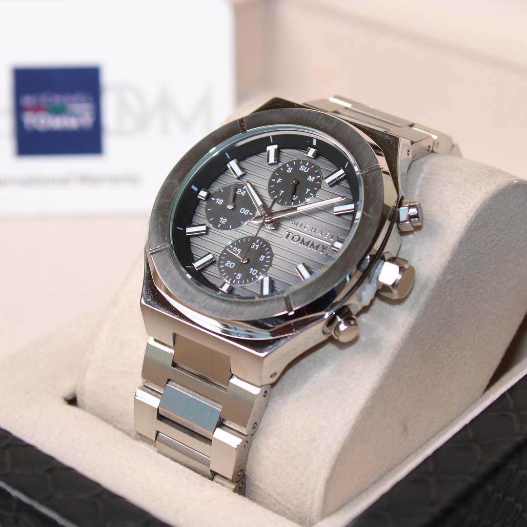 Silver watch with a detailed face on a white cushion, brand logo visible in the background