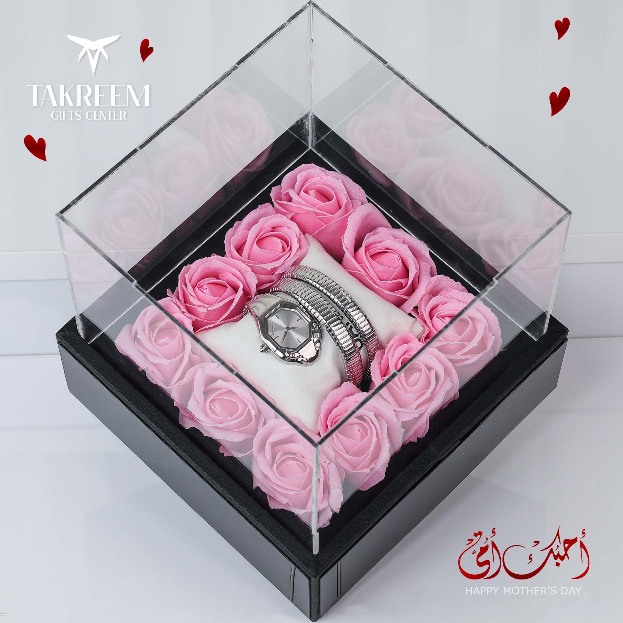 Silver watch on pink roses in a clear box with 'Takreem Gifts Center' branding.