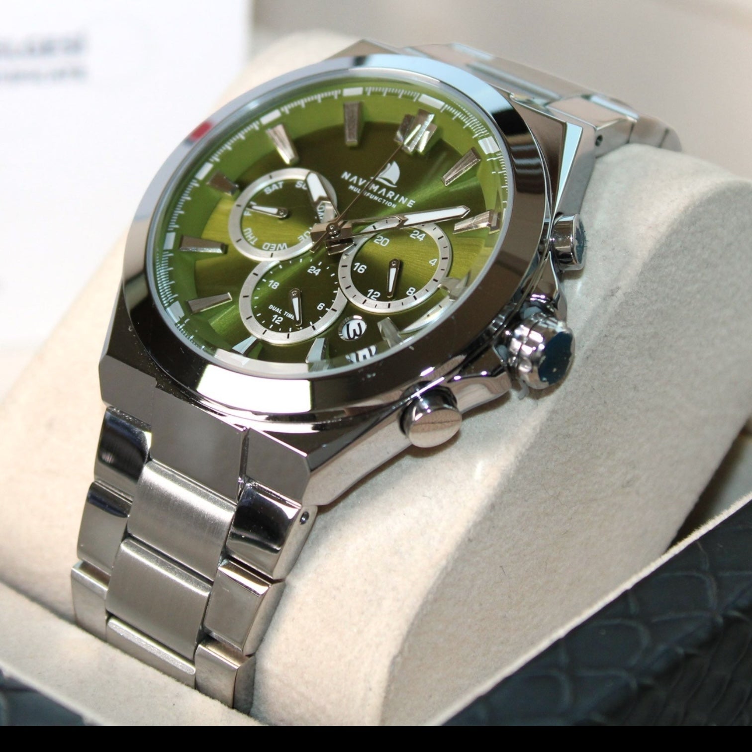 Silver watch with a green face on a white cushion
