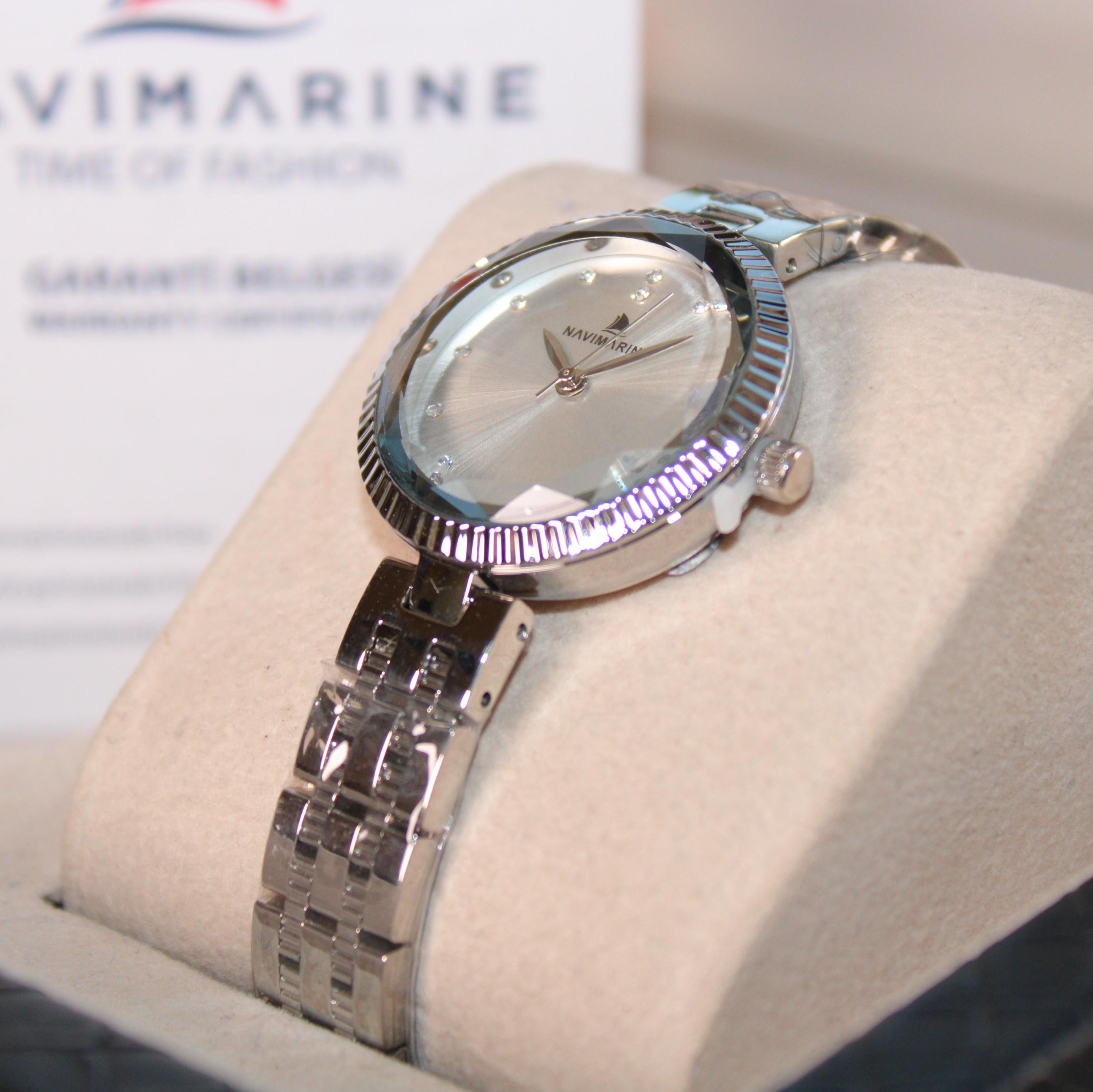 Silver wristwatch on a display stand with 'Navimagine' branding in the background