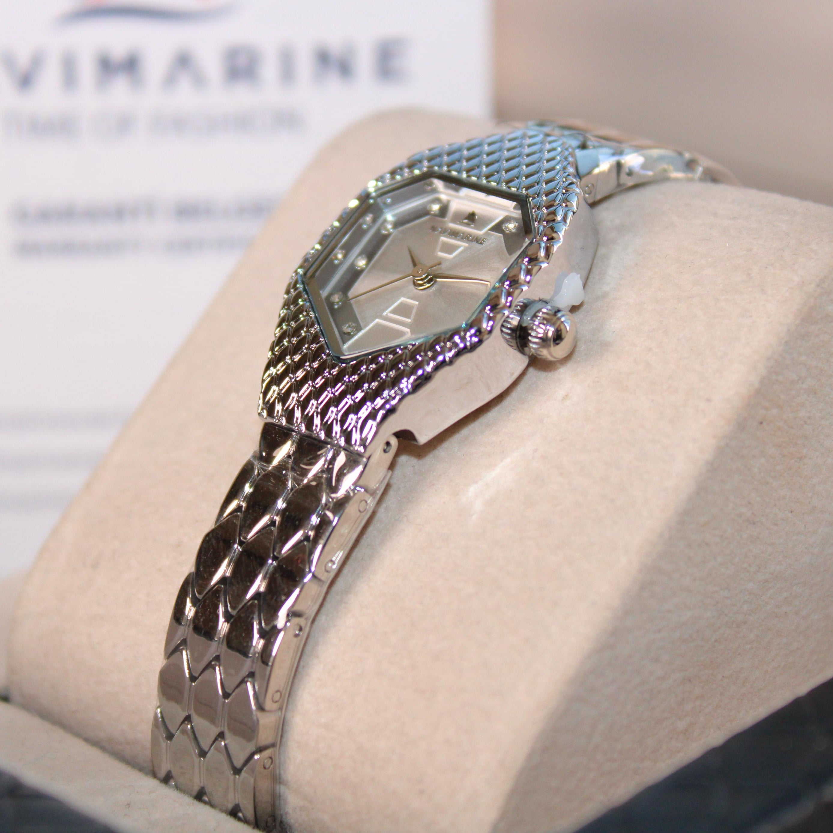 Silver watch on a display stand with a blurred Navimagine background