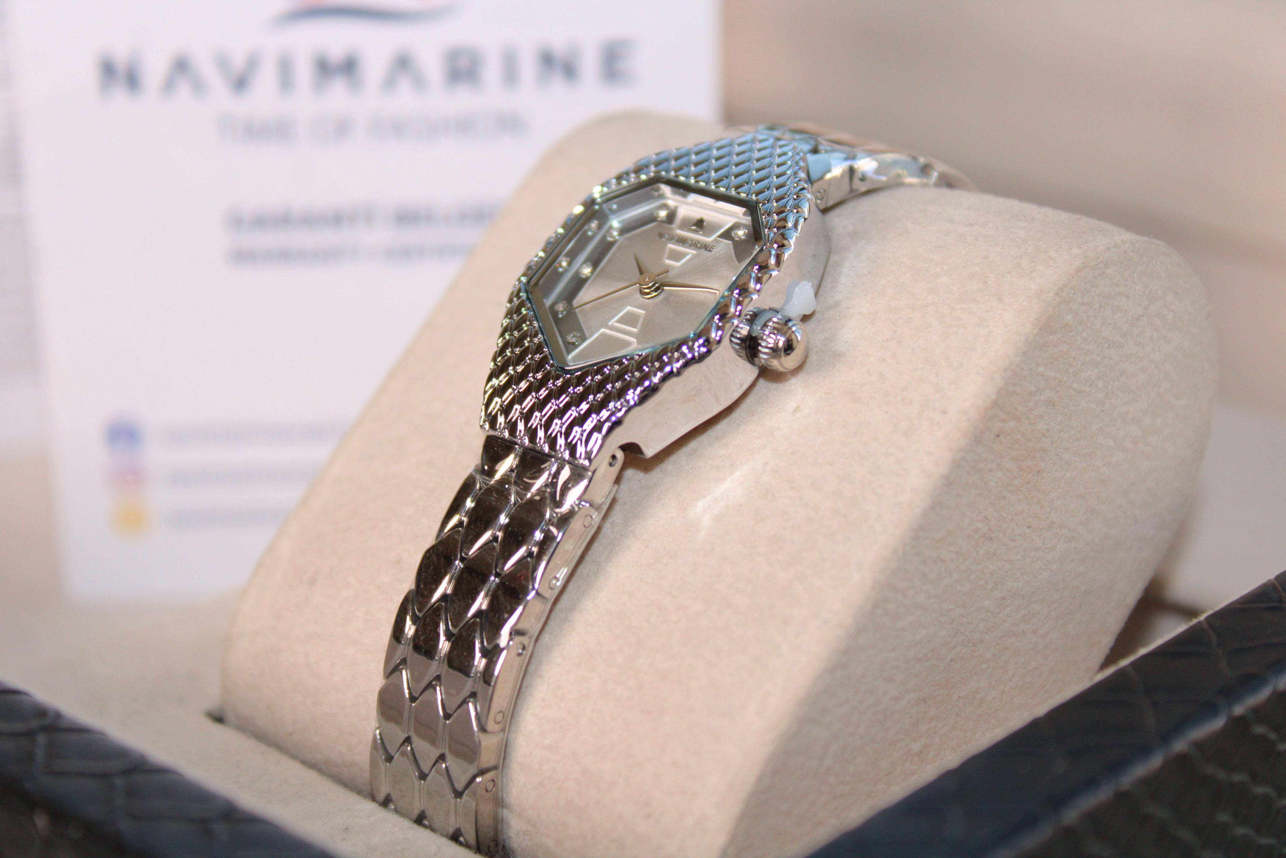 Silver watch on a display stand with a blurred Navimagine background