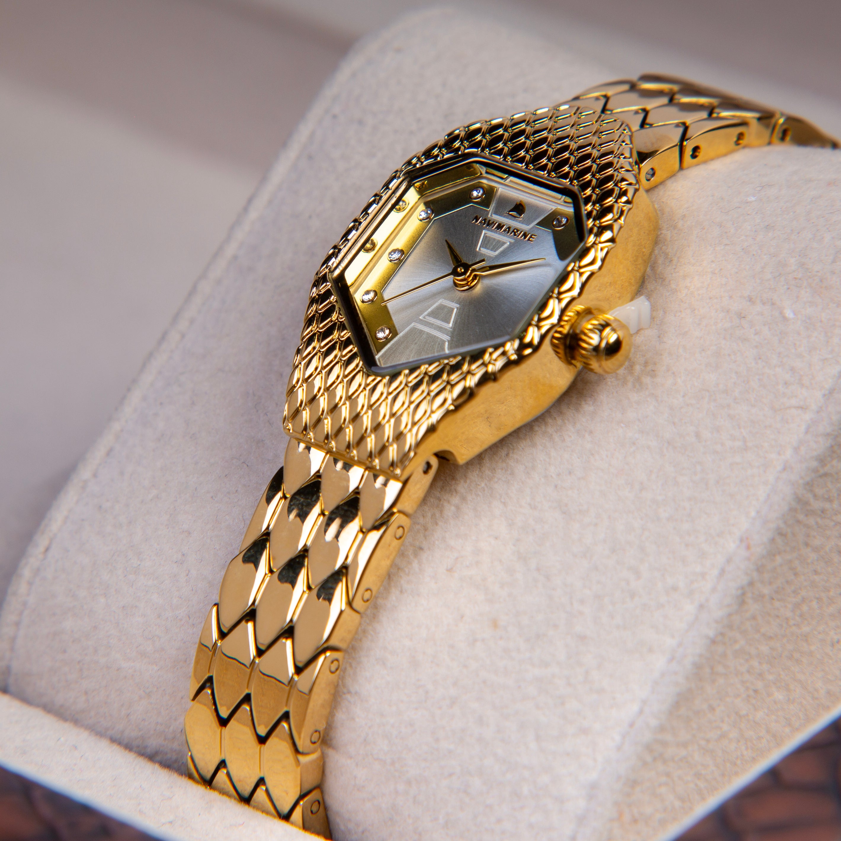 Gold wristwatch with intricate design on a light gray cushion