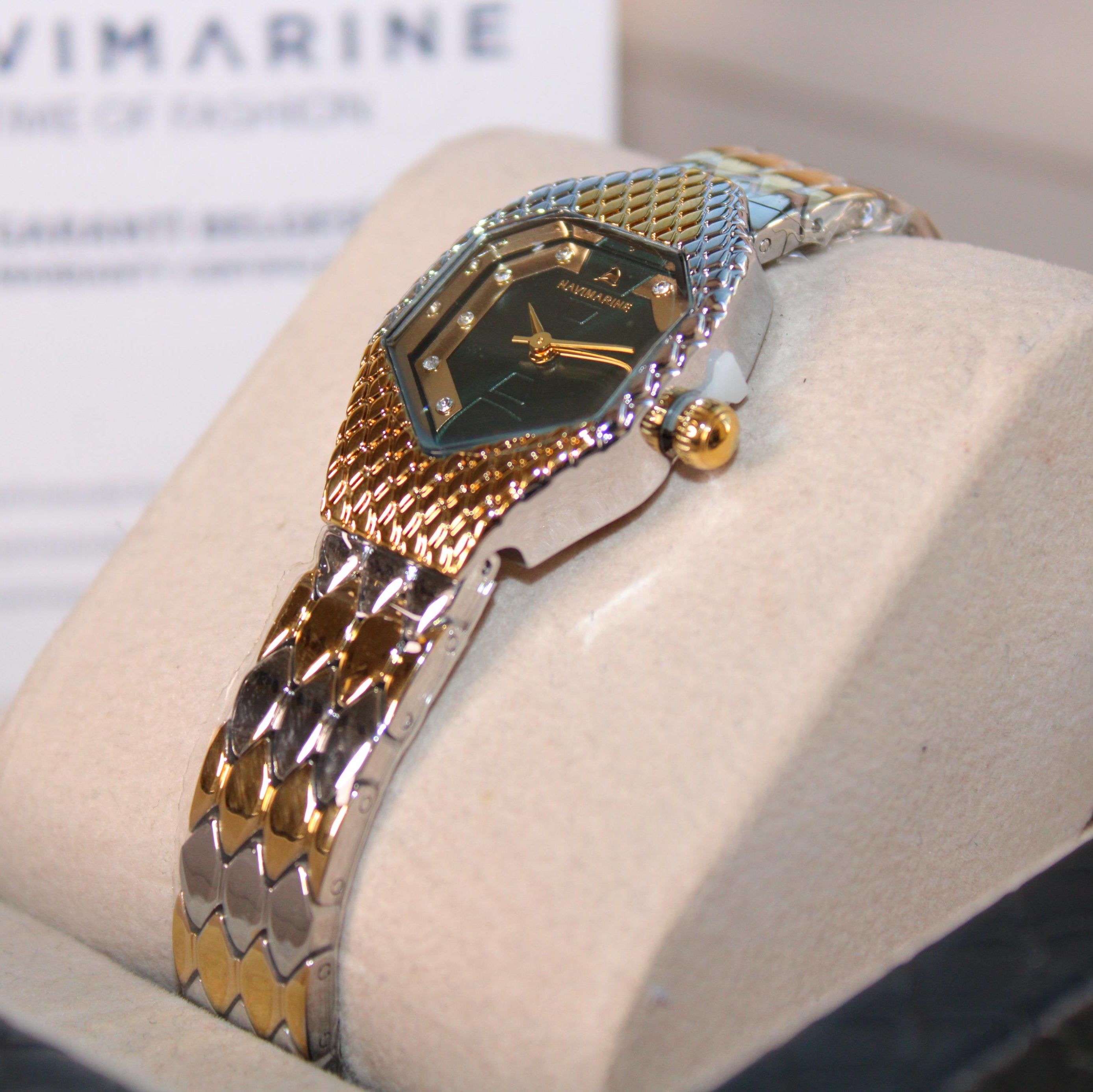 Gold and silver watch on a display stand with 'Navimagine' branding in the background.