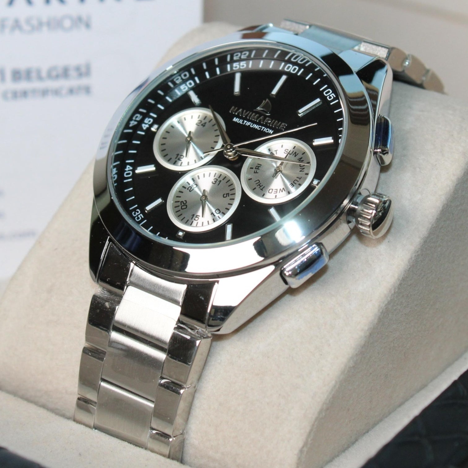 Silver watch with black dial on a white cushion, brand name visible