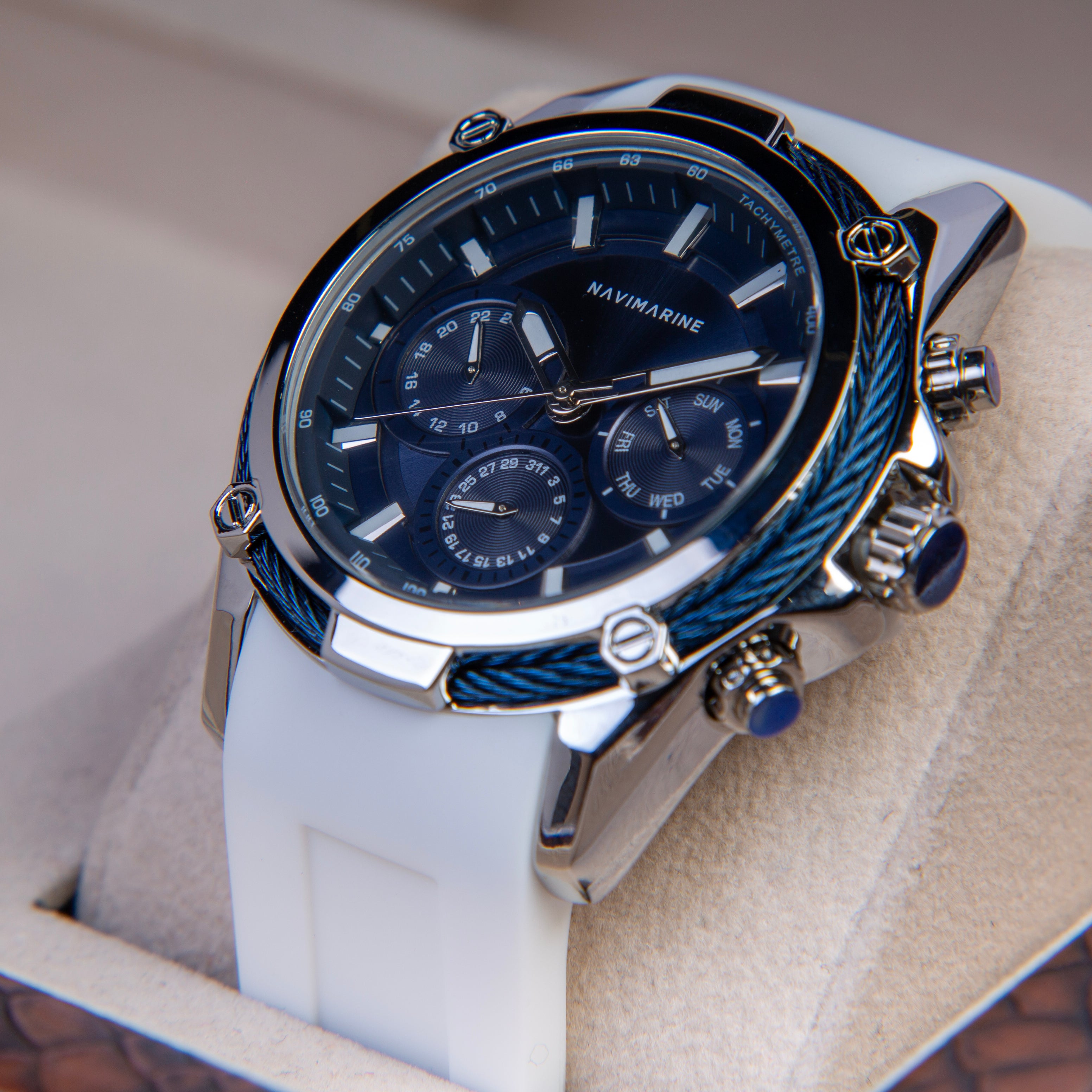 Luxury watch with blue face and white strap on a beige surface