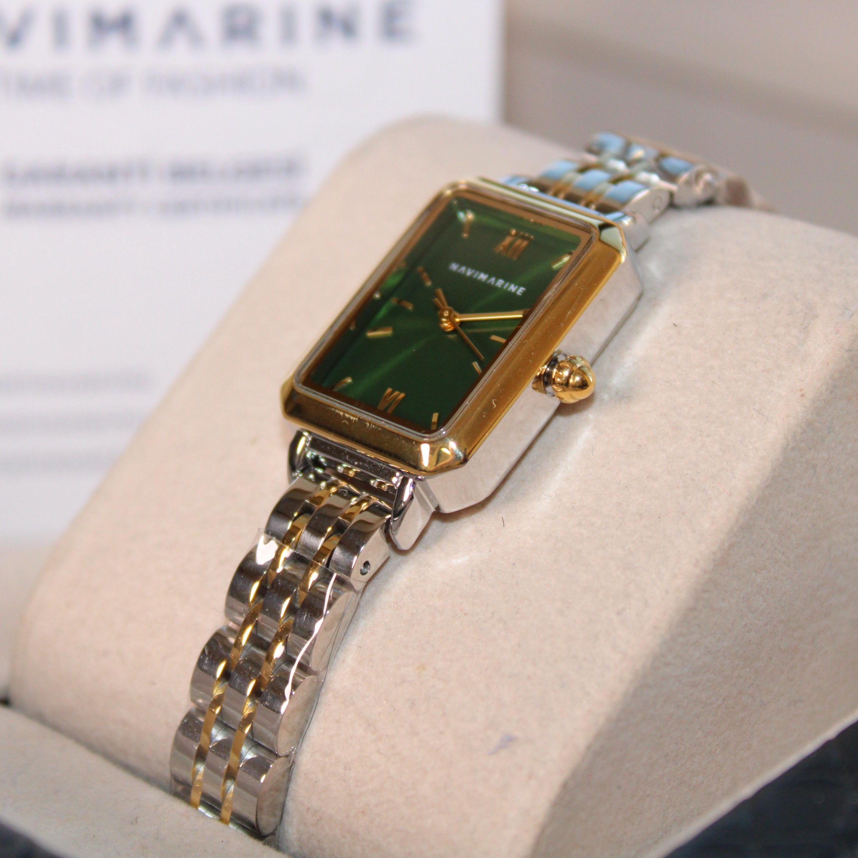 Gold and silver watch with green face on a display stand