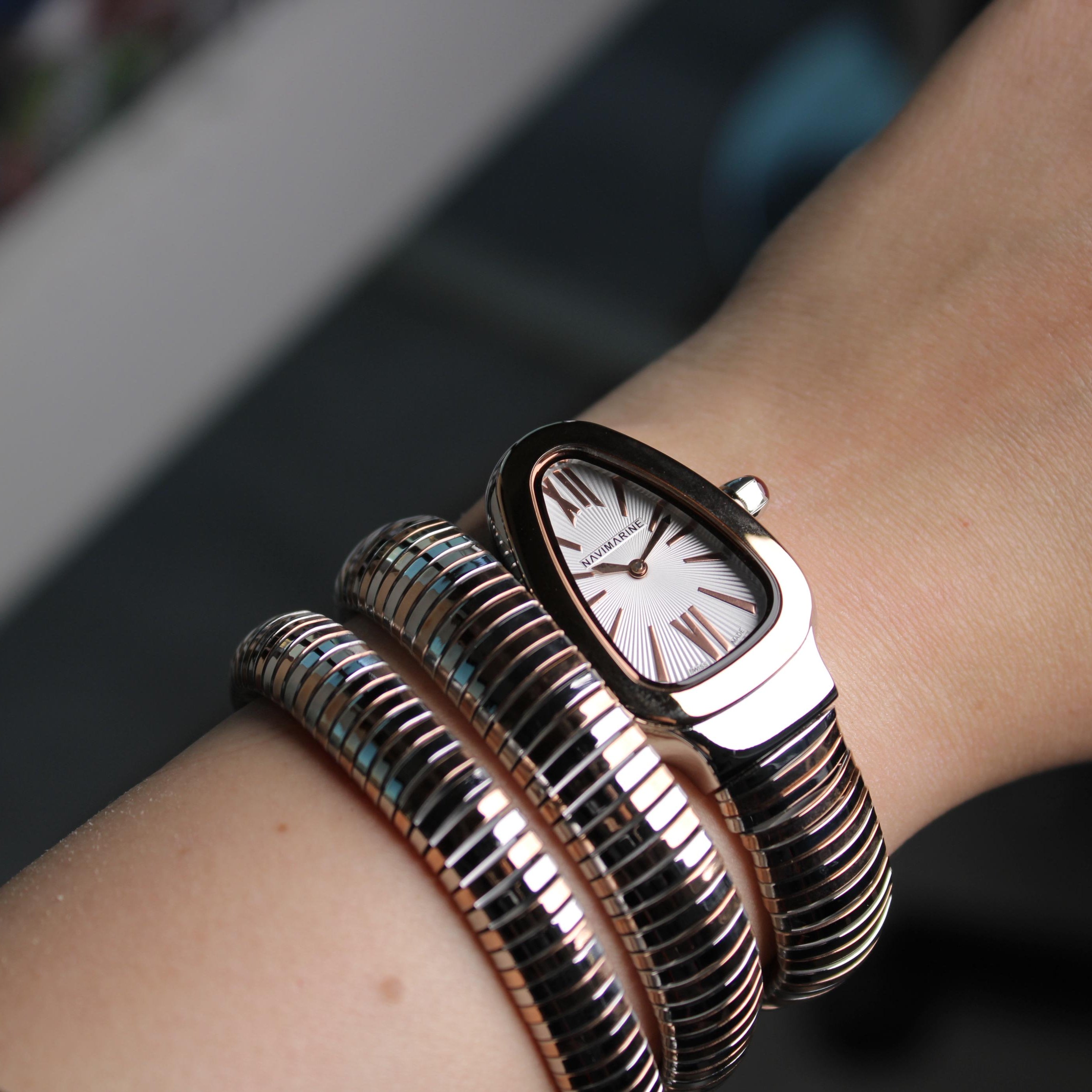 Silver watch with multiple bracelets on a wrist against a blurred background