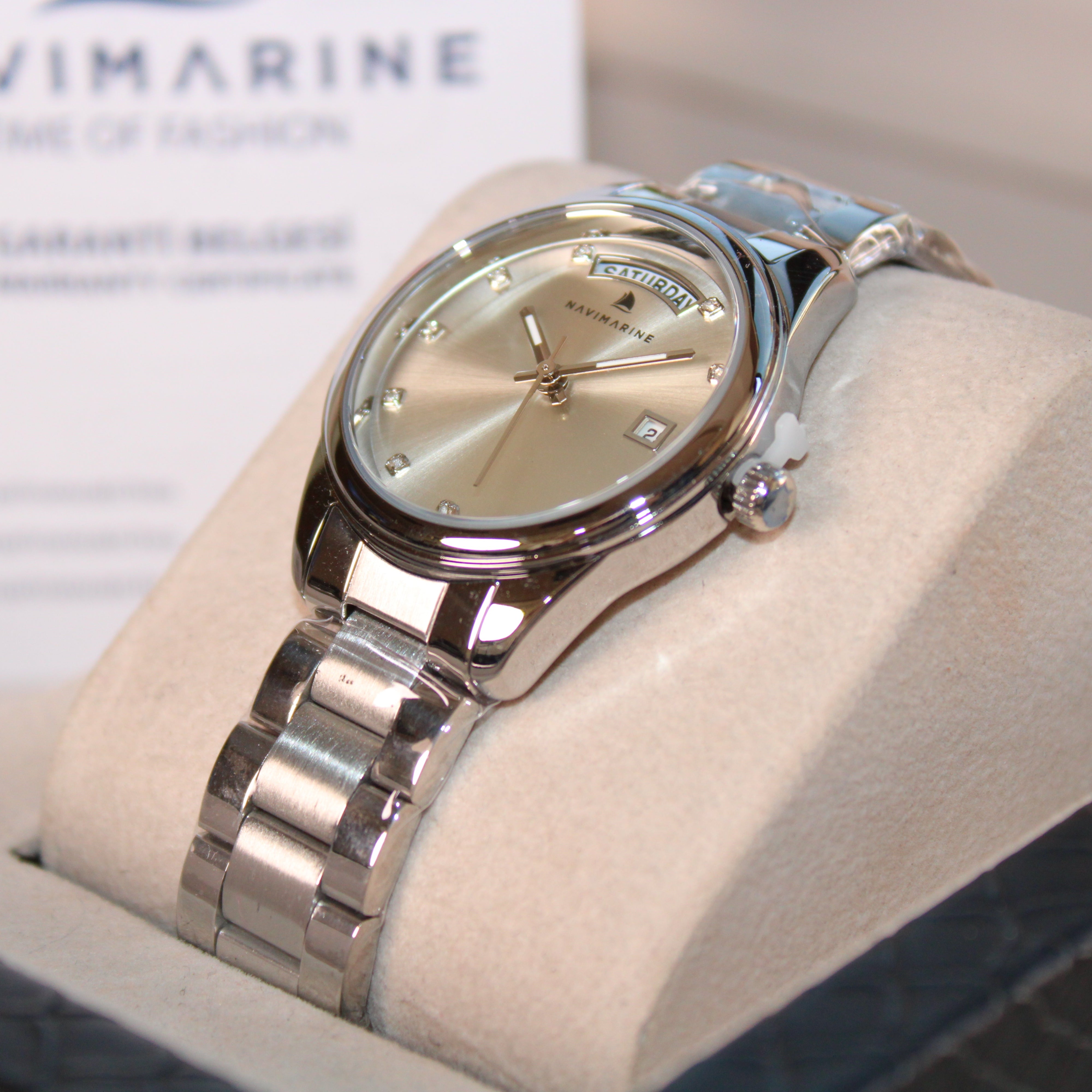 Silver wristwatch with beige face on a white cushion, brand 'Navimagine' visible