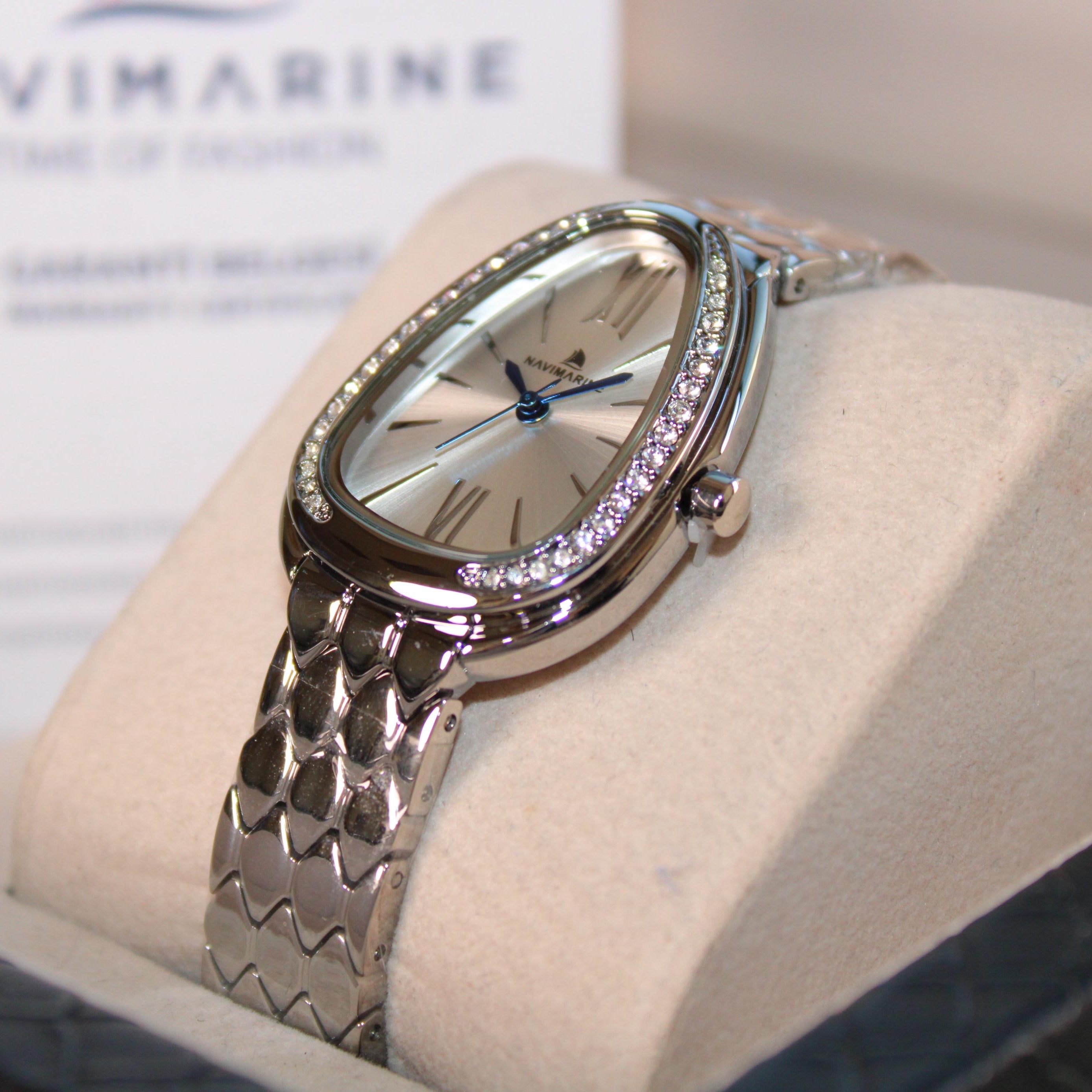 Silver watch on a white cushion with 'Navimagine' branding in the background