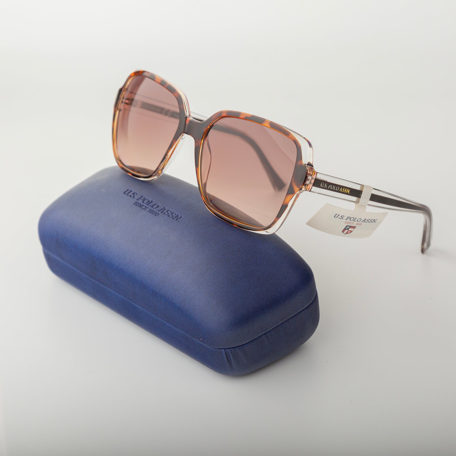 Sunglasses with a tortoiseshell frame and brown lenses on a blue case against a light gray background.