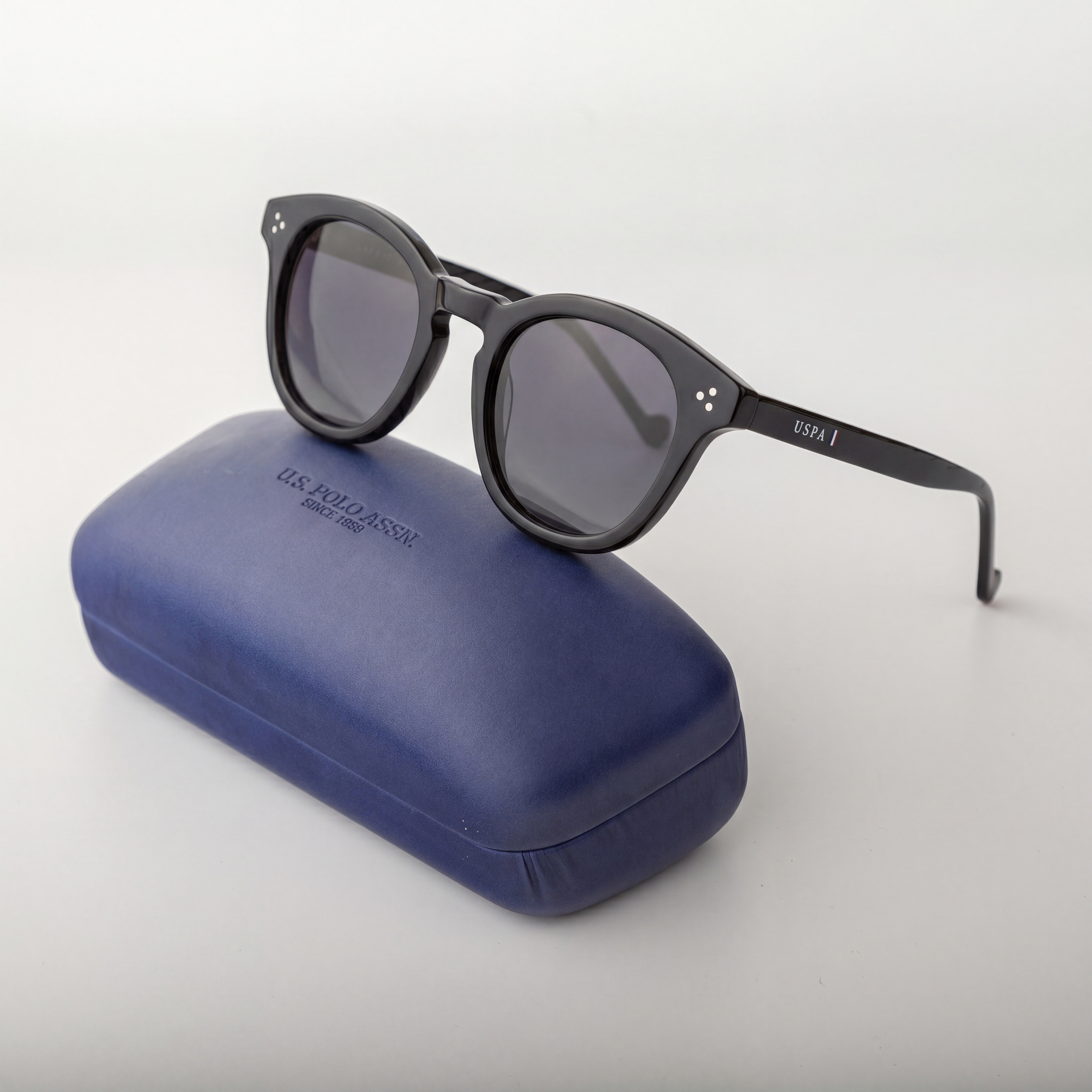 Black sunglasses on a blue case with 'LACOSTE' branding on a white background