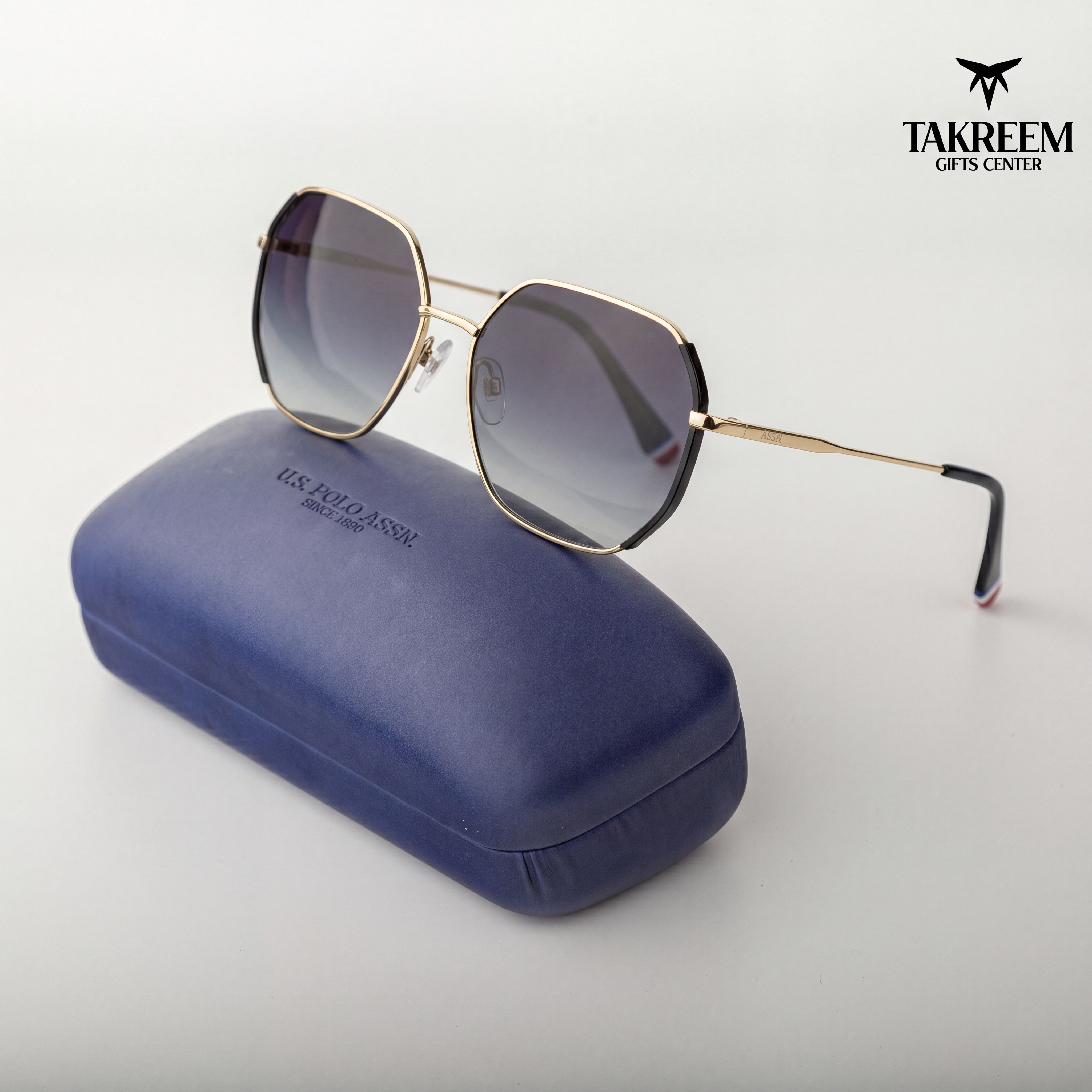 Sunglasses with gold frame and gradient lenses on a blue case, branded 'Takreem Gifts Center'.