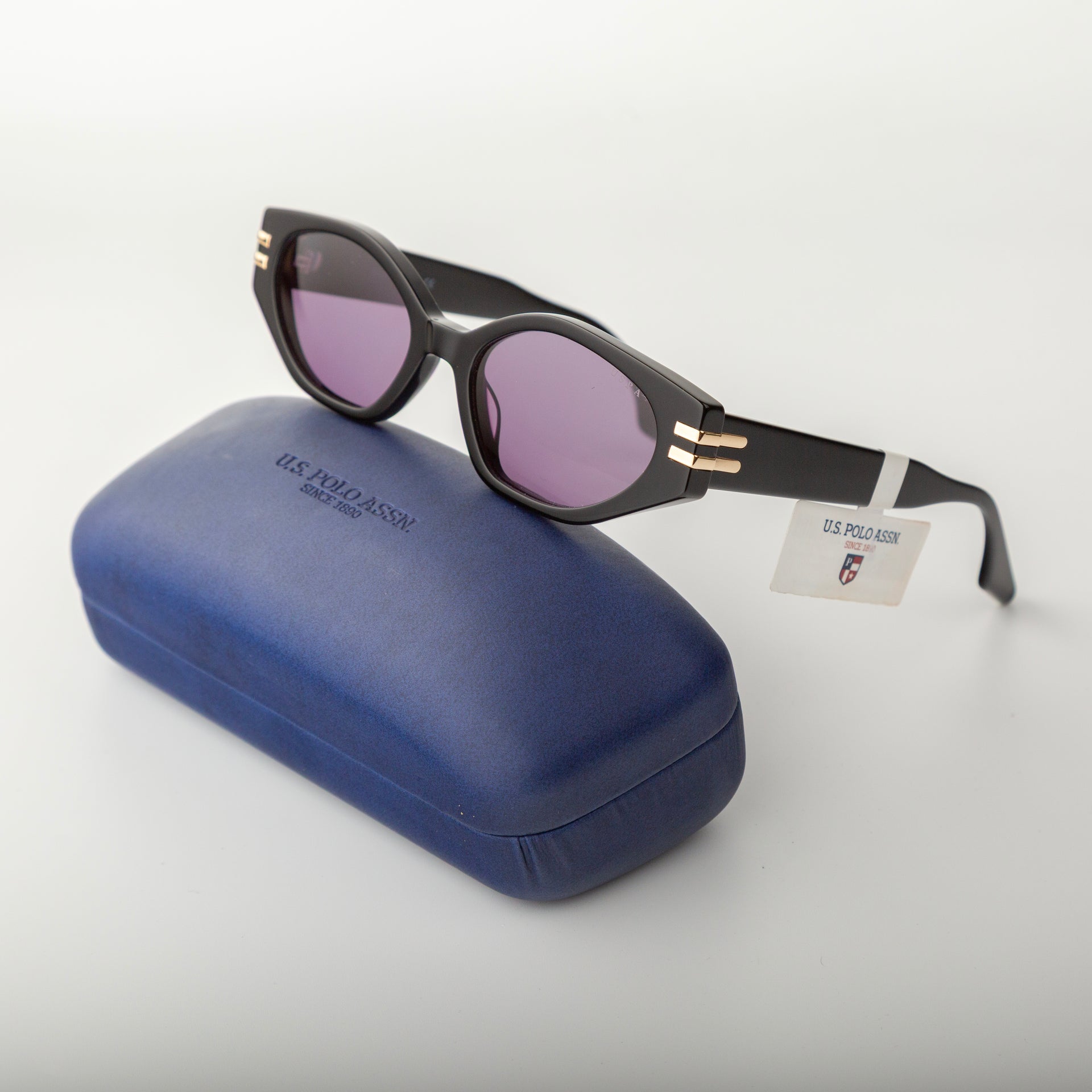 Sunglasses with purple lenses and gold accents on a blue case with 'U.S. Polo Assn.' branding.