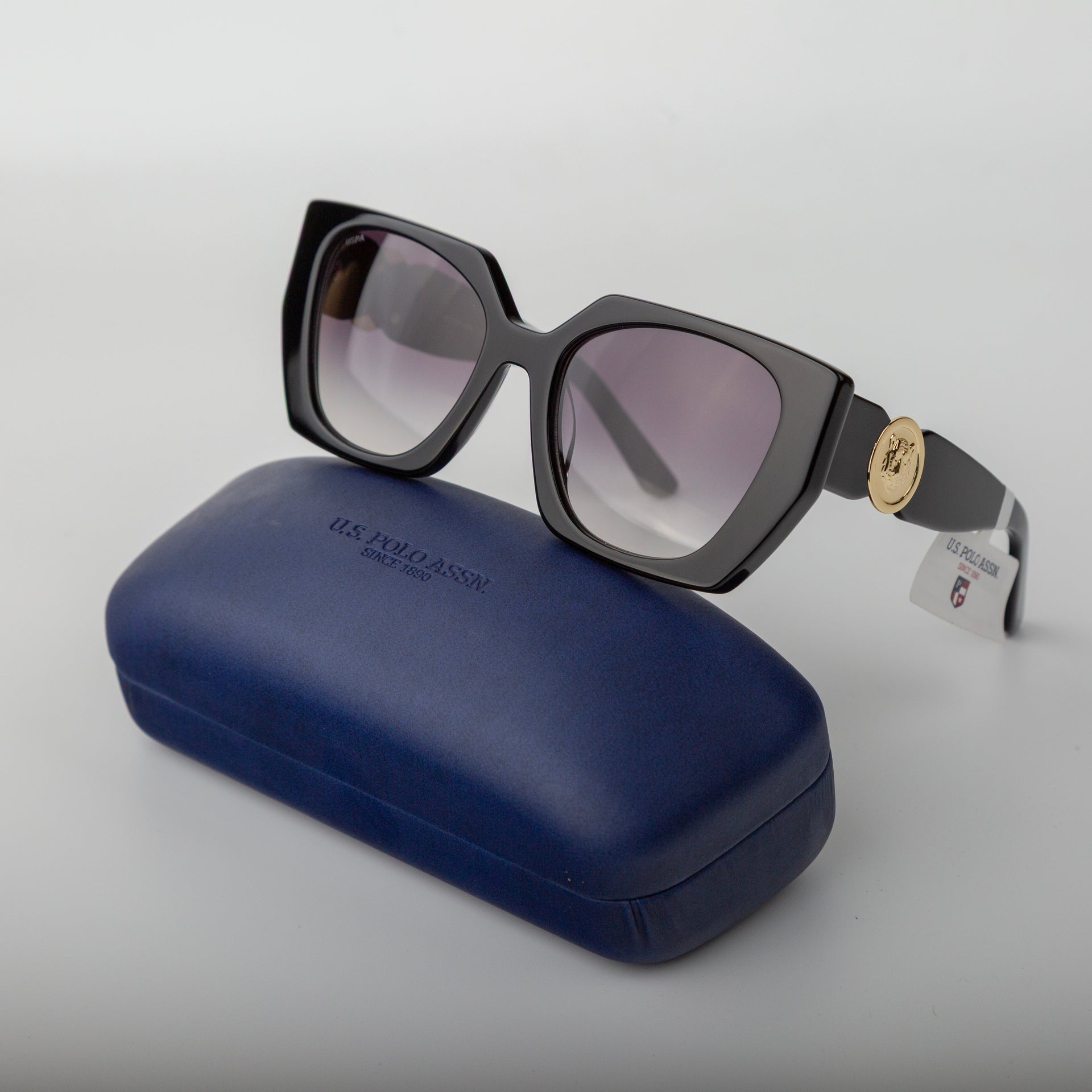 Black sunglasses with a gold logo on a blue case against a light gray background