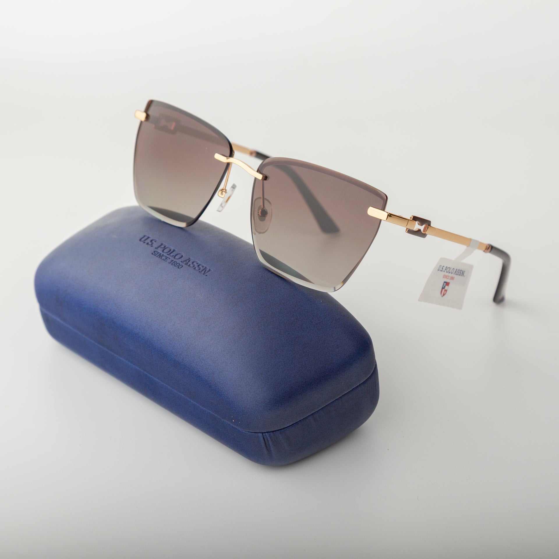 Sunglasses with gold frame and gradient lenses on a blue case with visible brand name.