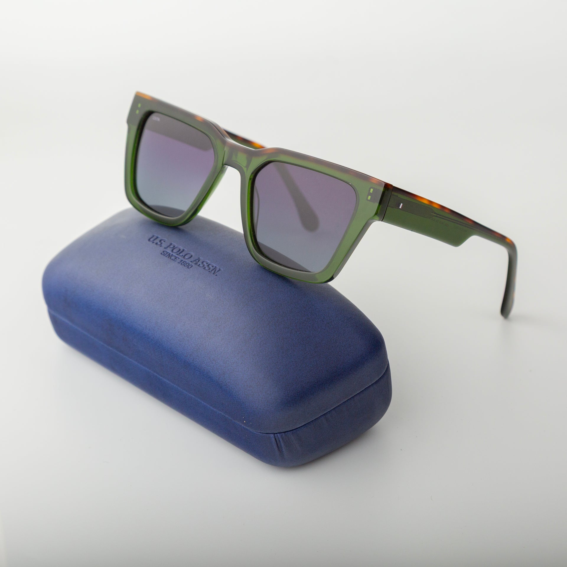 Green sunglasses with tortoiseshell accents on a blue case against a white background