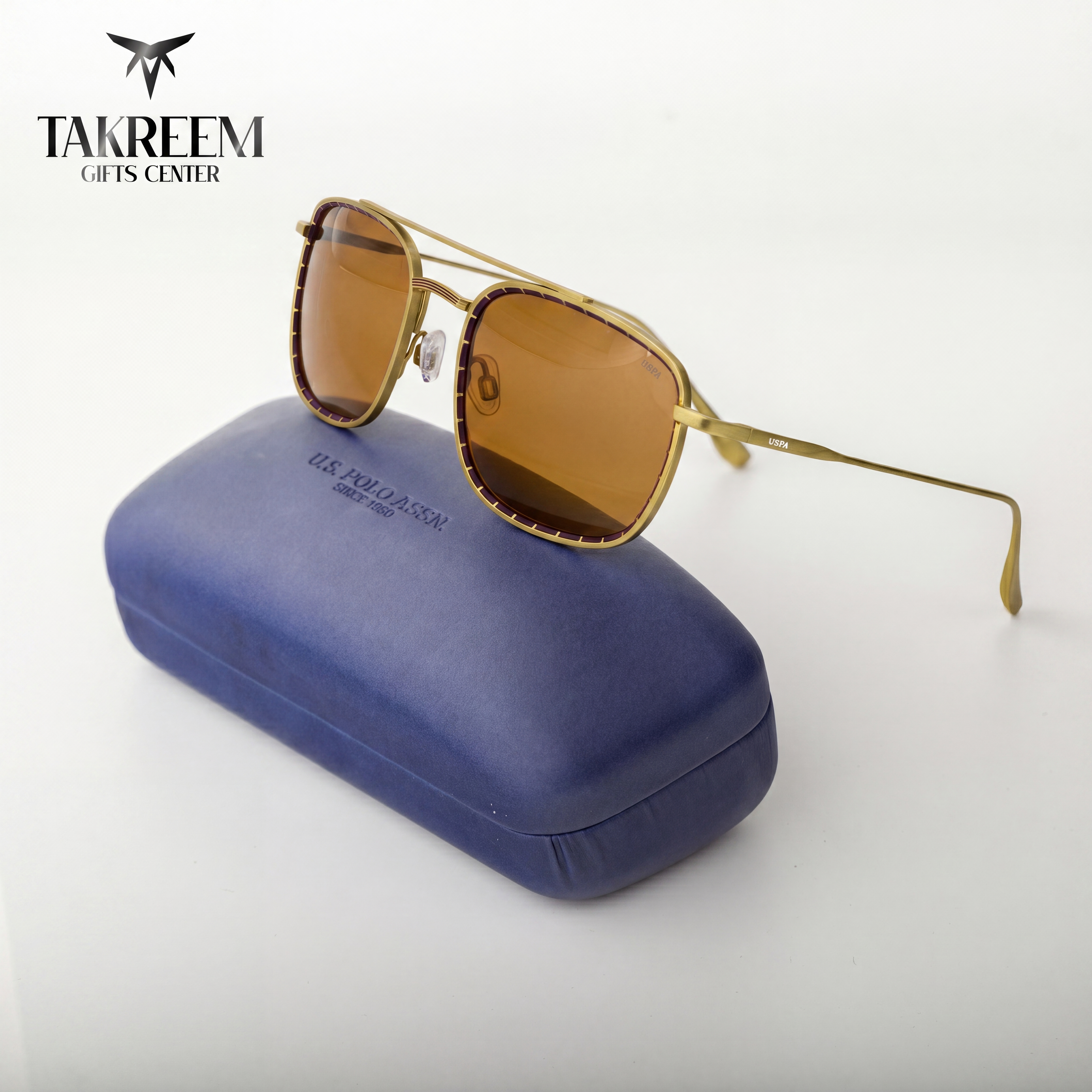 Gold sunglasses with brown lenses on a blue case, branded 'Takreem Gifts Center'.