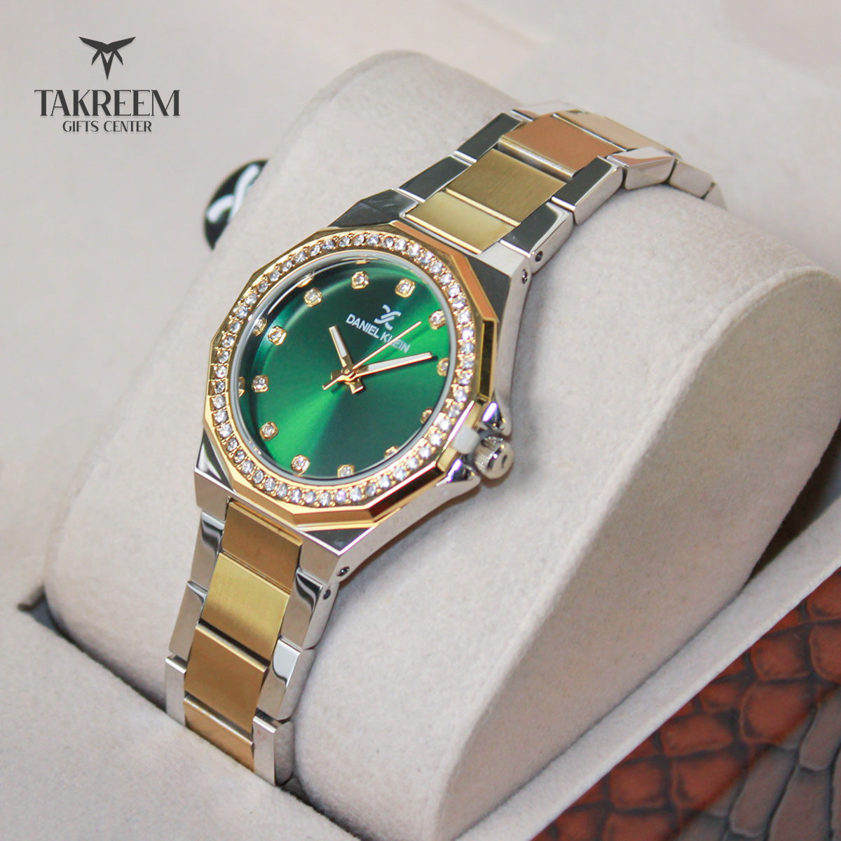 Luxury watch with green face and gold accents on a white cushion, branded 'Takreem Gifts Center'.