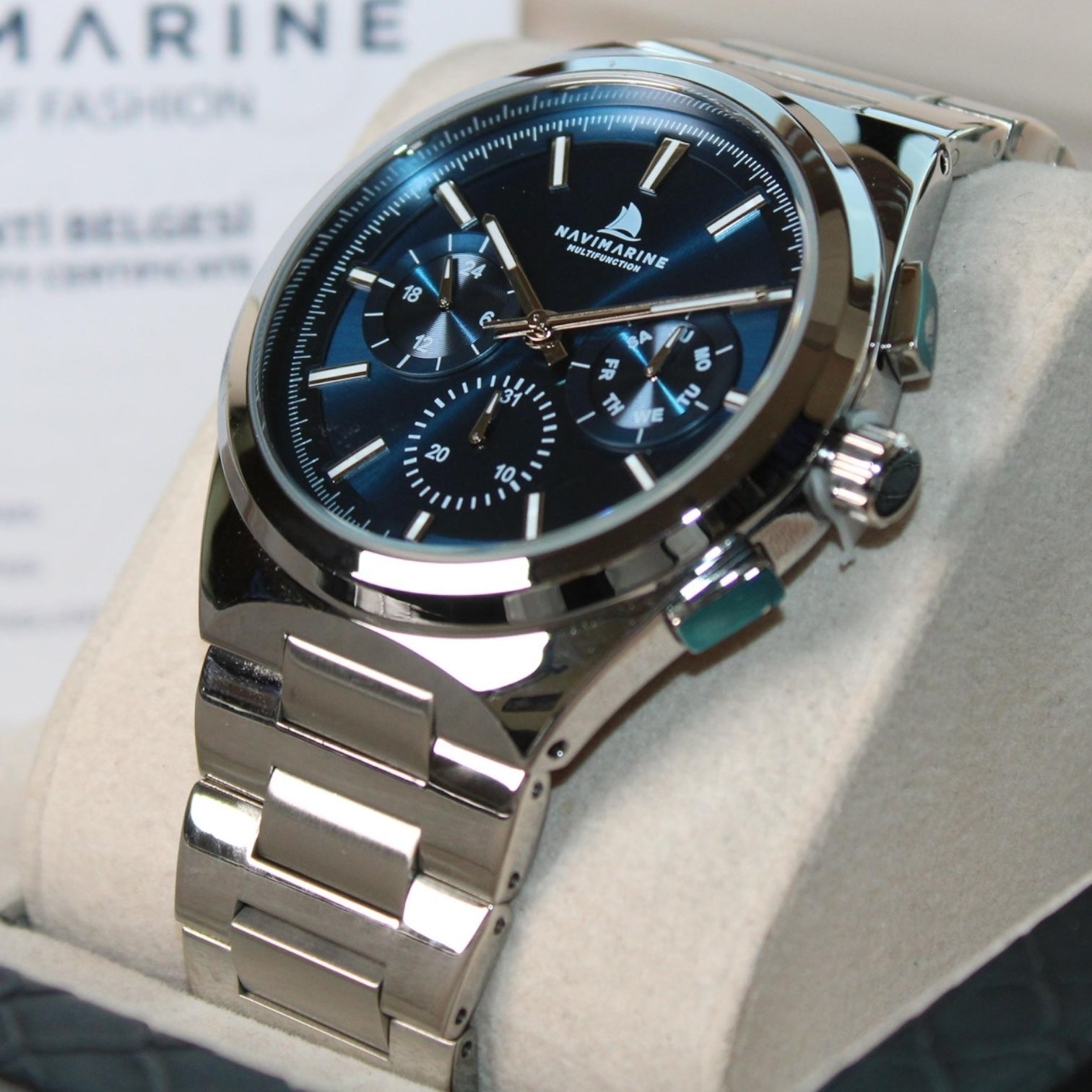 Silver watch with blue face on a light gray surface, brand 'Naviforce' visible