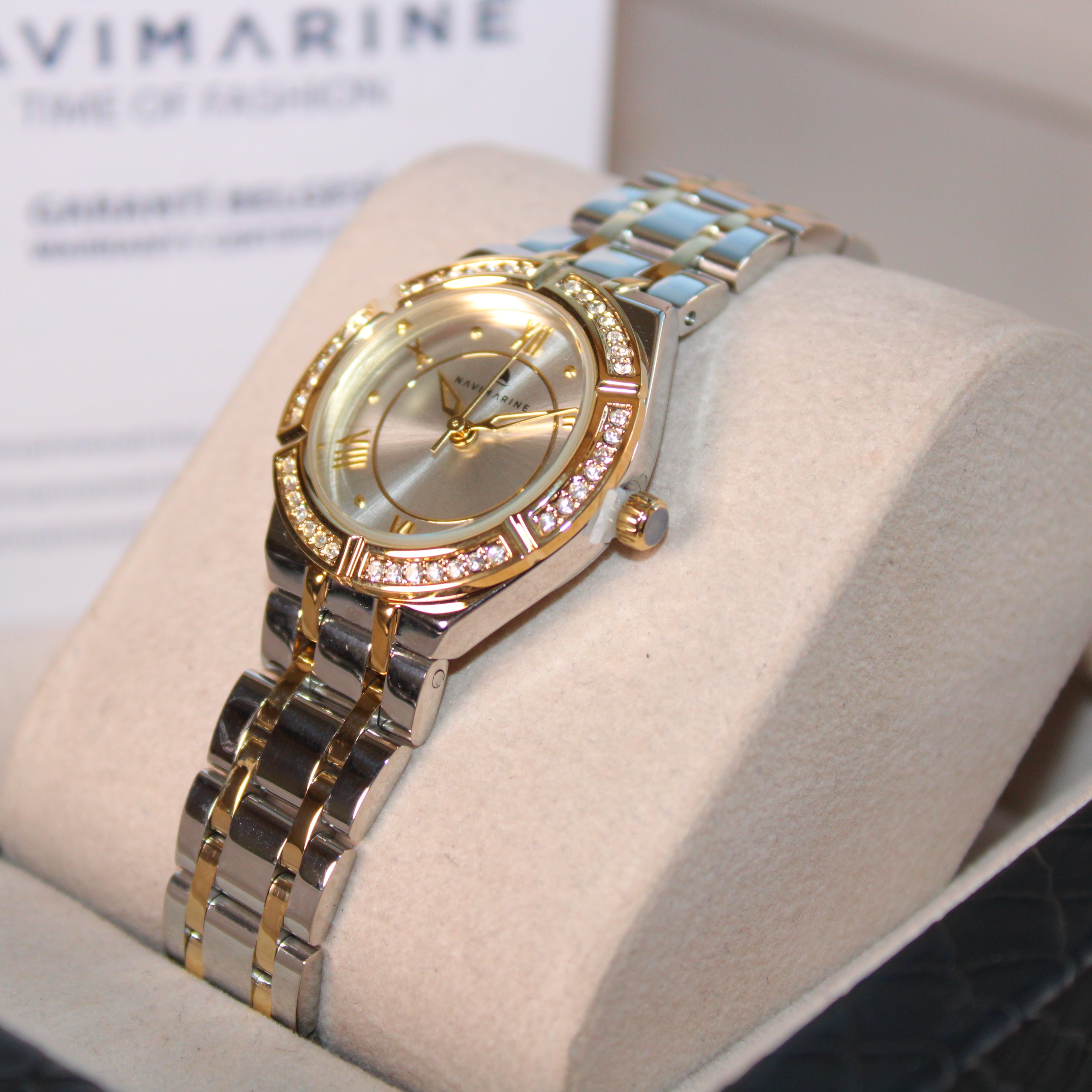 Gold and silver watch on a display stand with 'Navimagine' branding in the background.