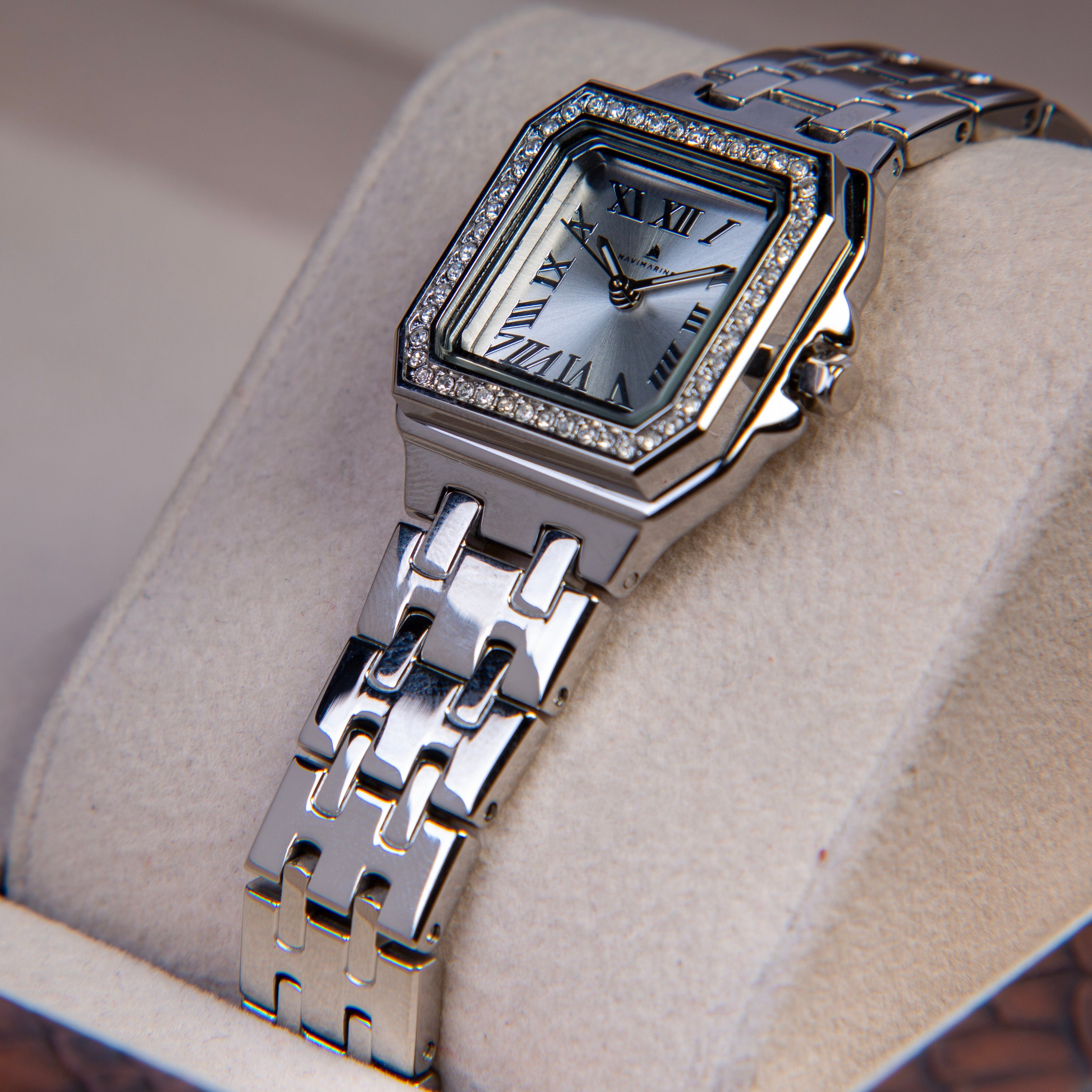 Silver wristwatch with diamond-studded case on a light brown cushion