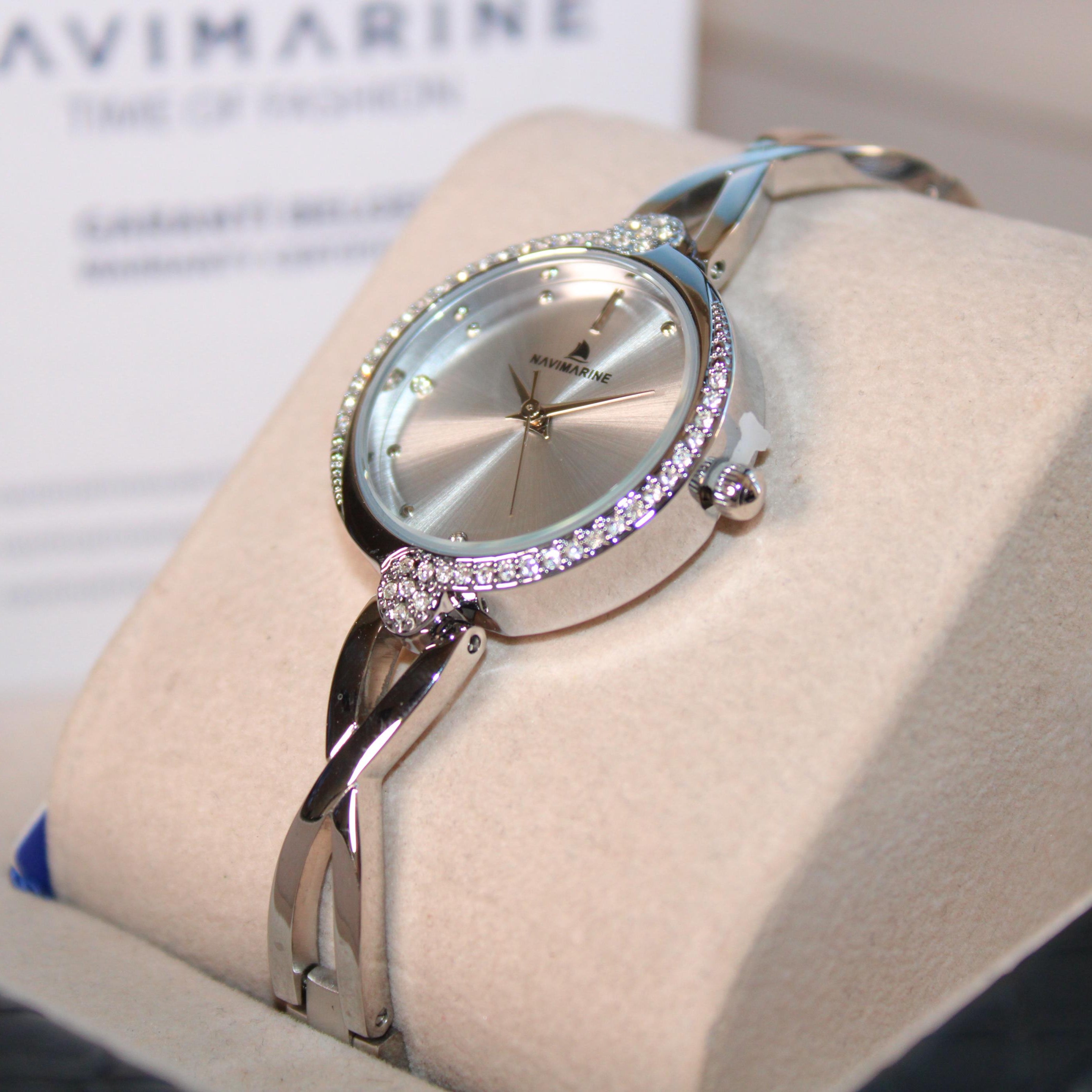 Silver watch with pink accents on a white cushion, brand 'NaviMarine' visible