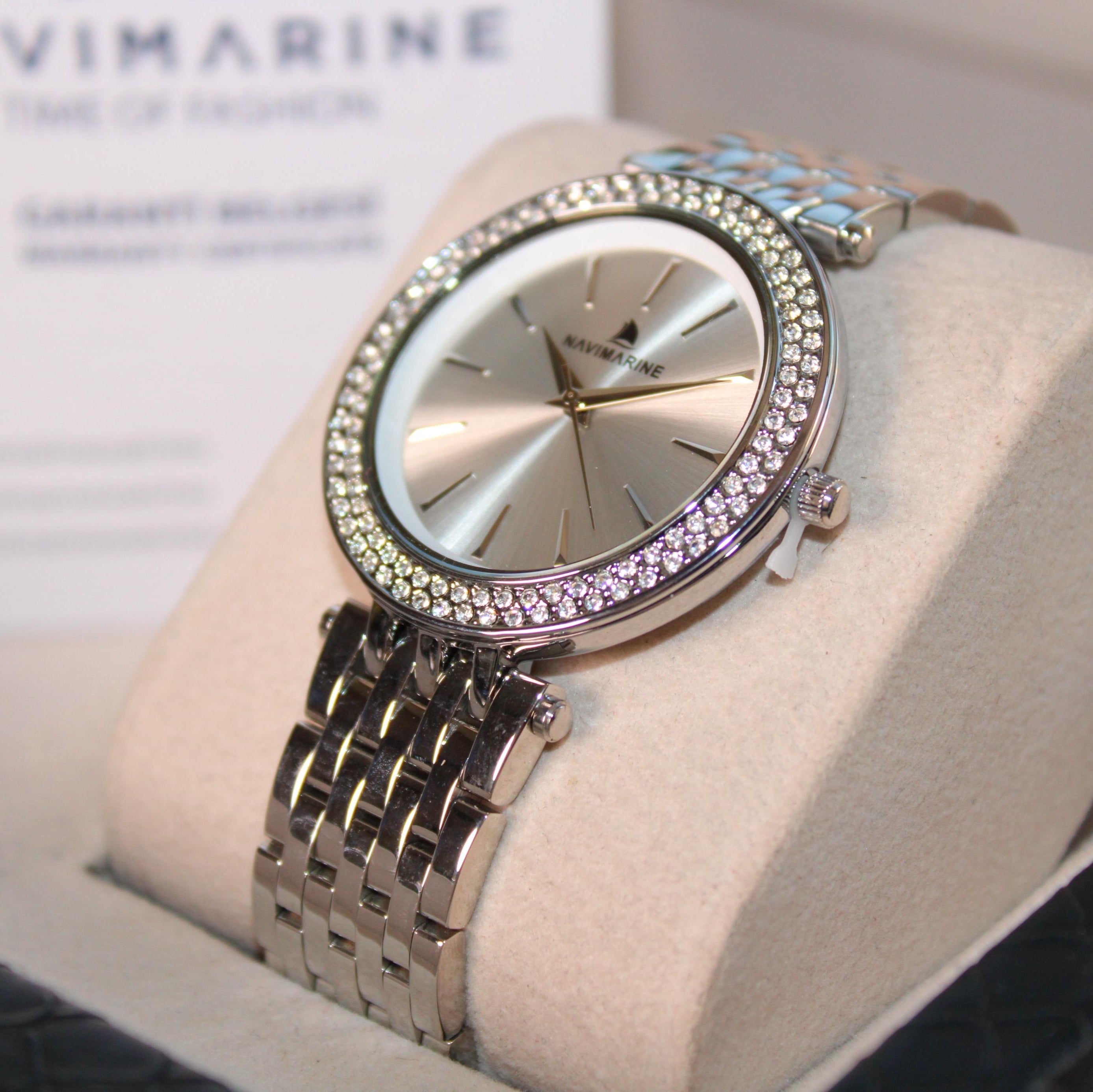 Silver watch with gemstone accents on a beige cushion, brand 'NaviMarine' visible