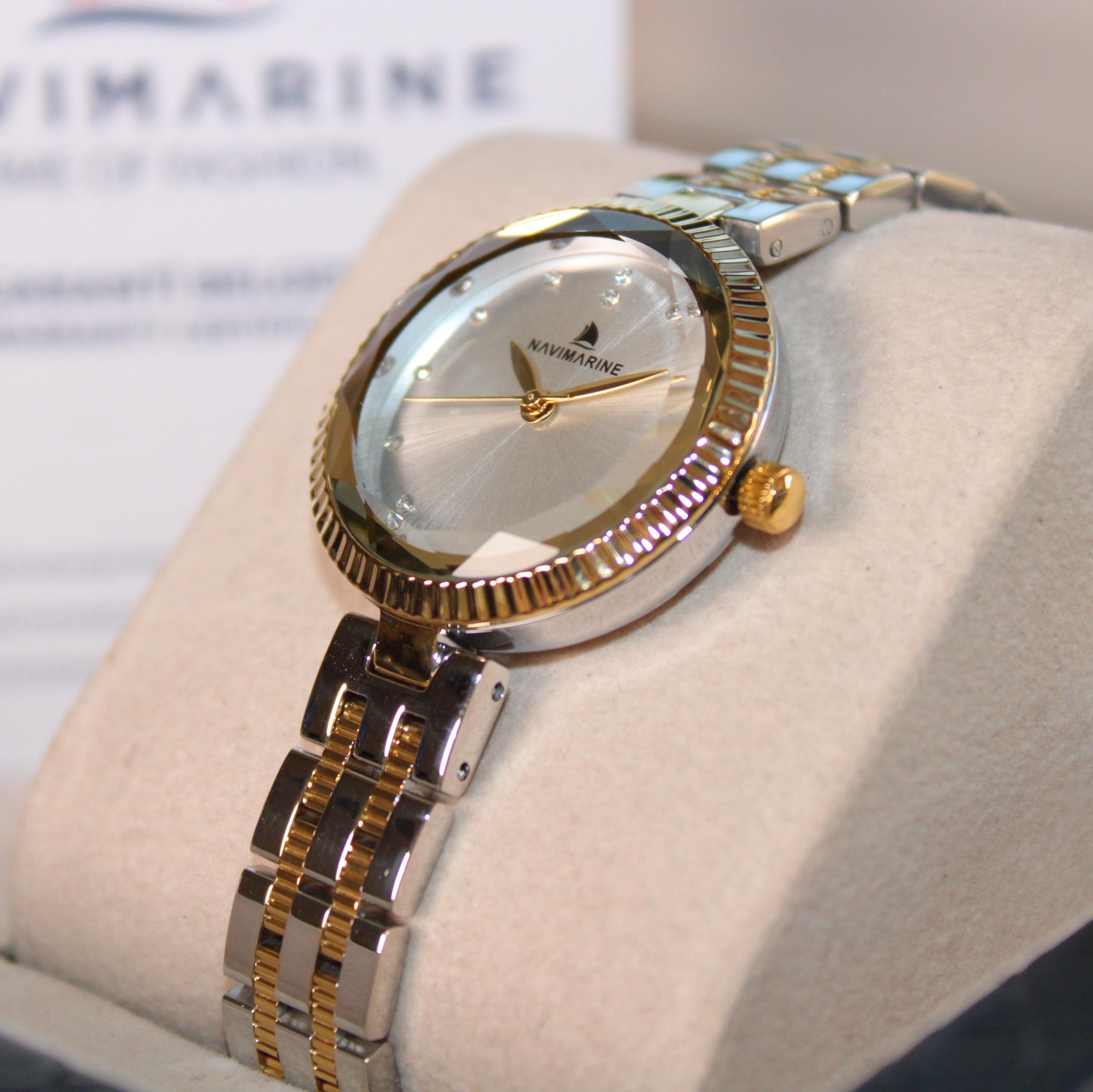 Gold and silver watch on a display stand with 'Navimagine' branding in the background.