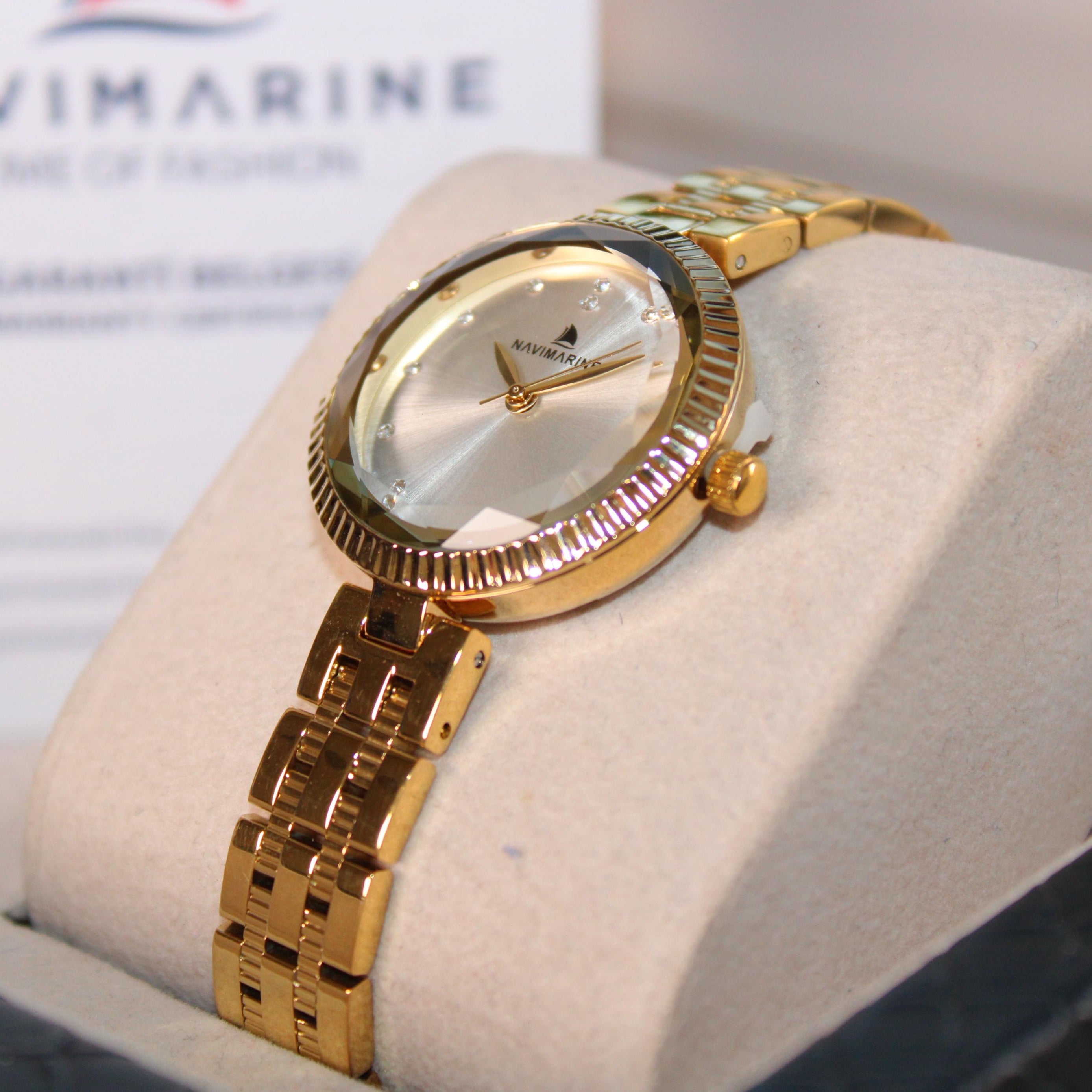 Gold wristwatch on a display stand with 'Navimagine' branding in the background