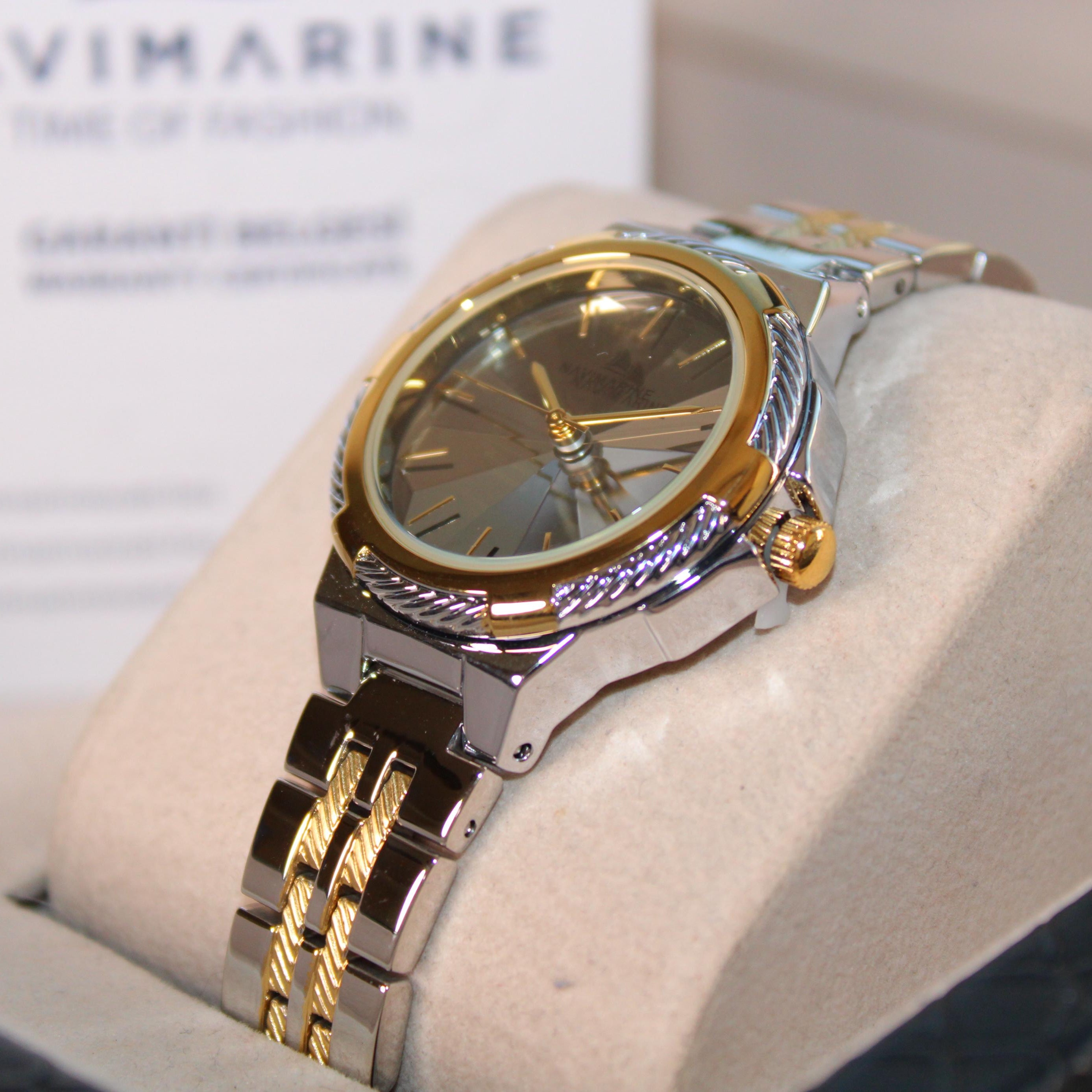 Gold and silver watch on a display stand with 'Navimagine' branding in the background.