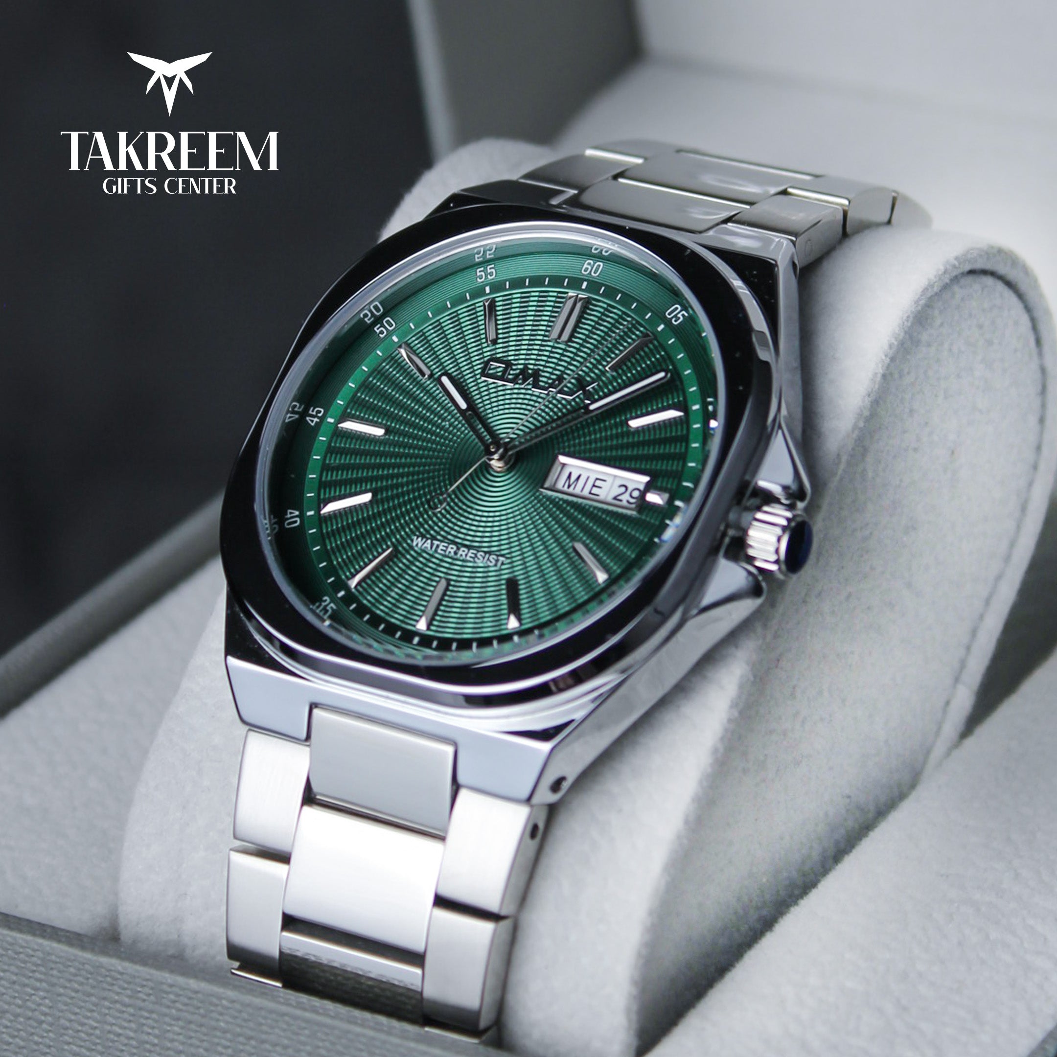 Silver watch with green dial on a gray cushion, branded 'Takreem Gifts Center'.