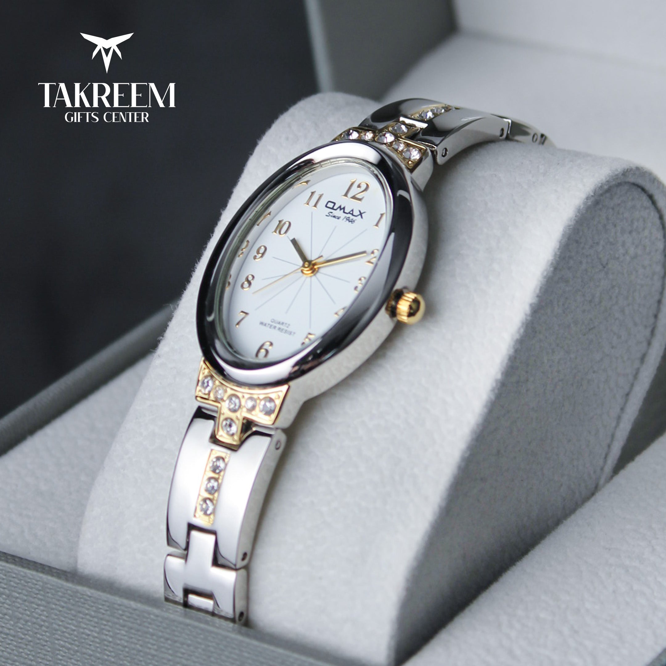 Silver and gold watch with white face on a gray cushion, brand 'Takreem' visible