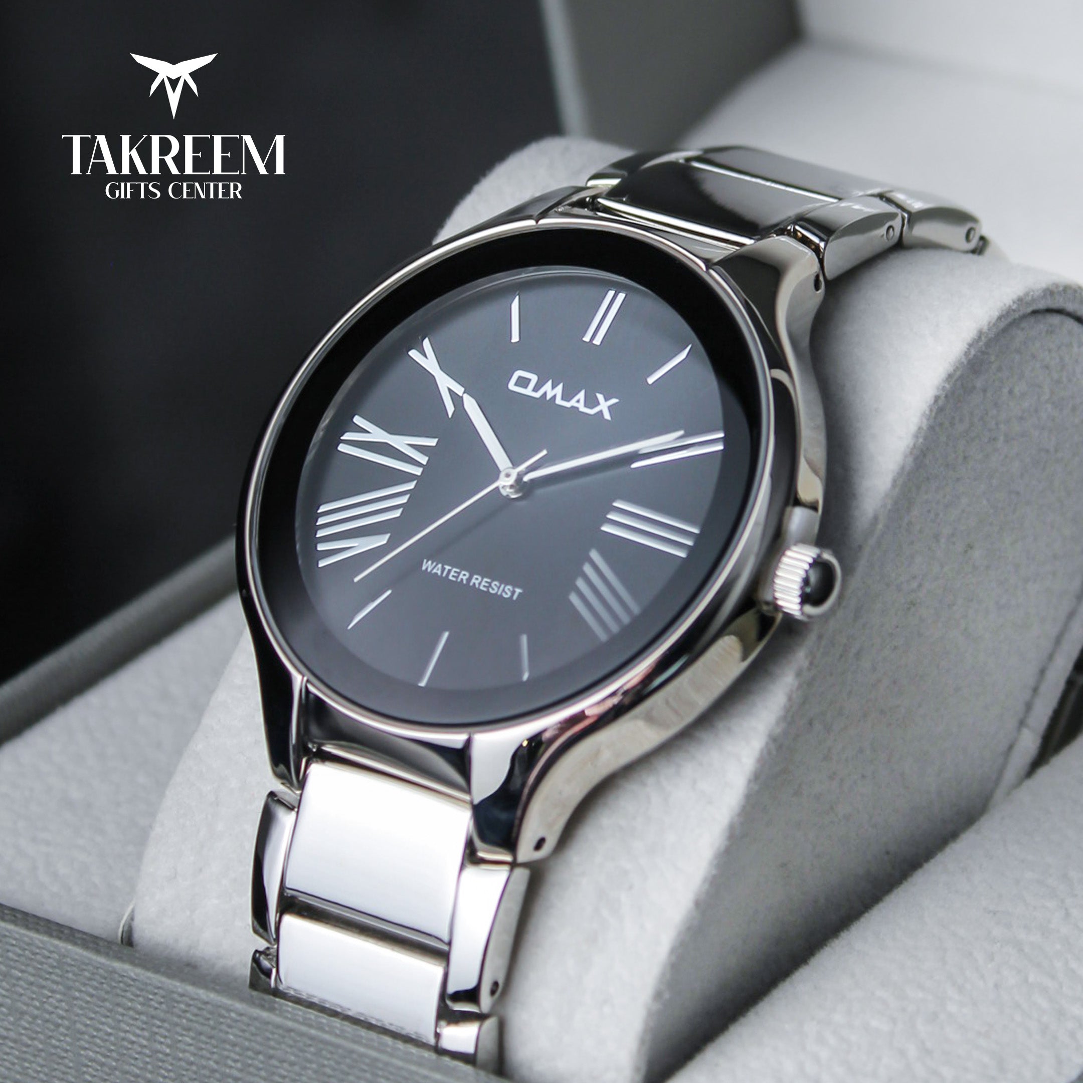 Silver watch with black dial on a gray cushion, branded 'Takreem Gifts Center'.