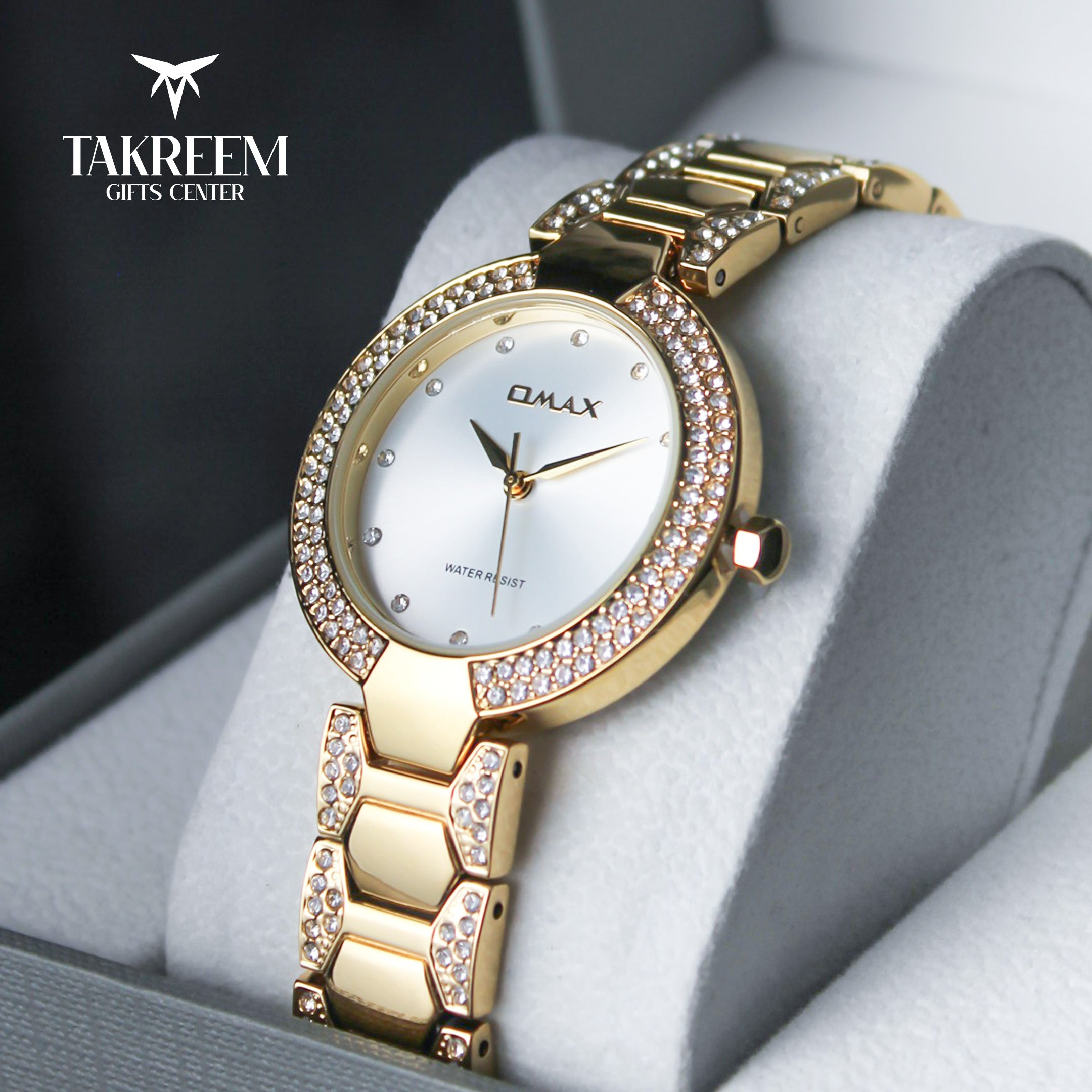 Gold wristwatch with decorative band on a gray cushion, branded 'Takreem Gifts Center'.