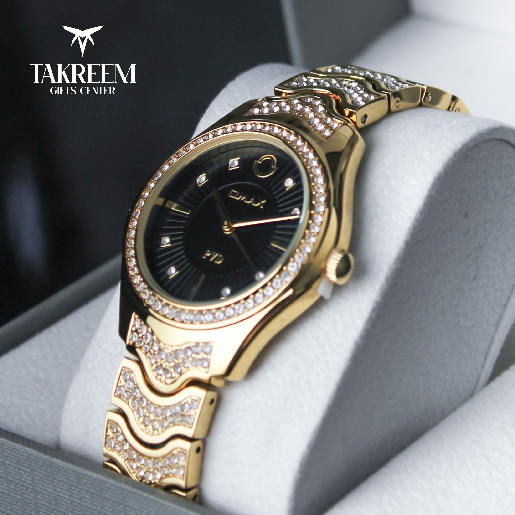 Gold wristwatch with decorative band on a gray surface, brand 'Takreem' visible.