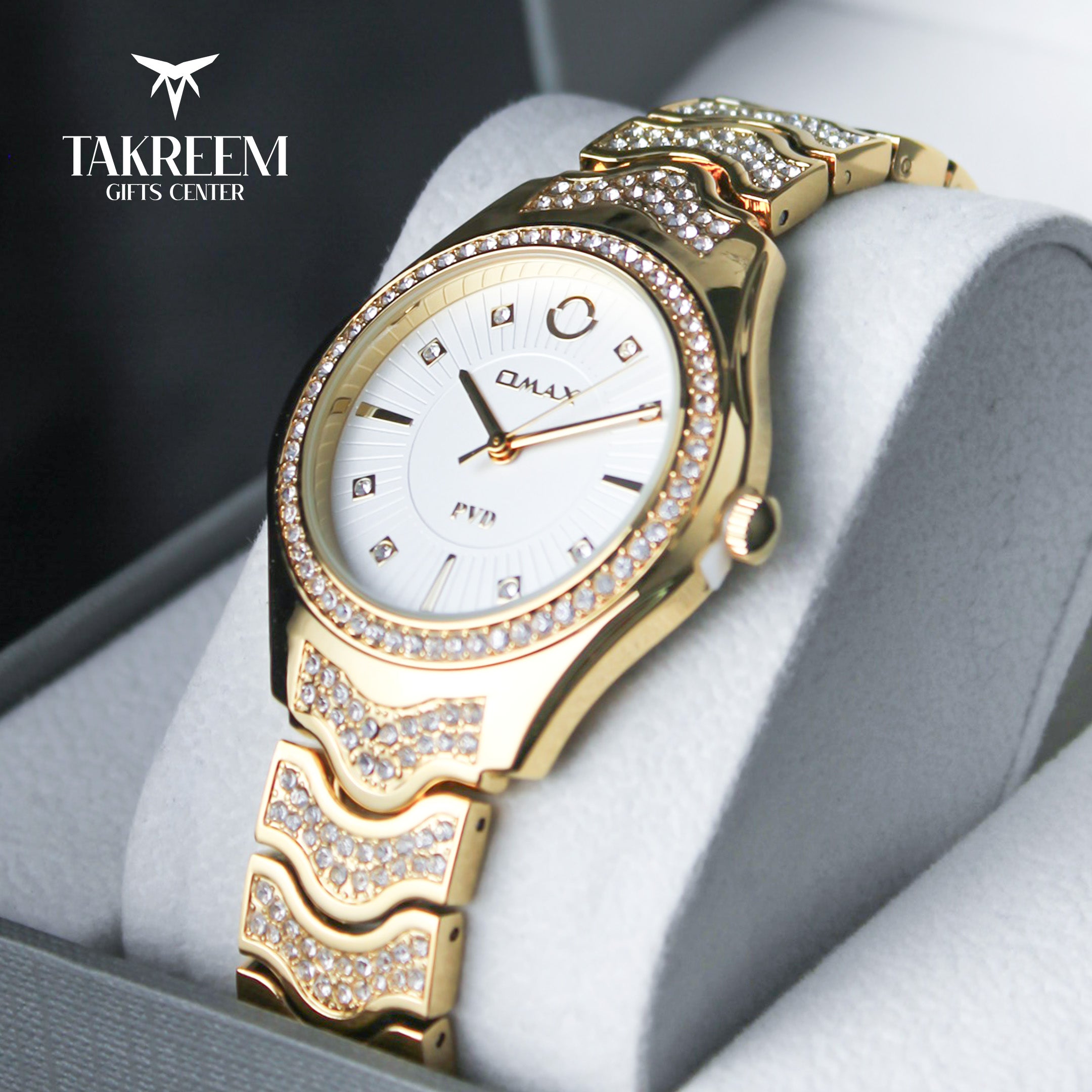 Gold wristwatch with decorative band on a gray surface, branded 'Takreem Gifts Center'.