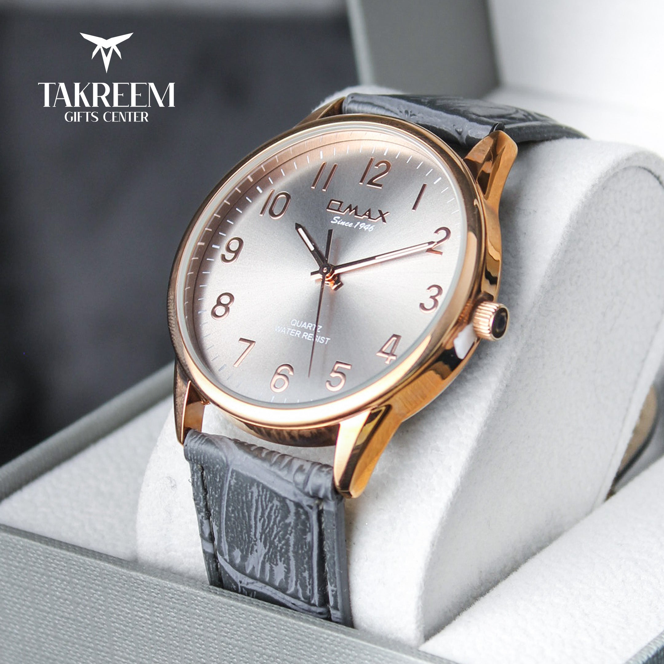 Wristwatch with gray strap and gold casing on a white cushion, brand 'Takreem' visible.