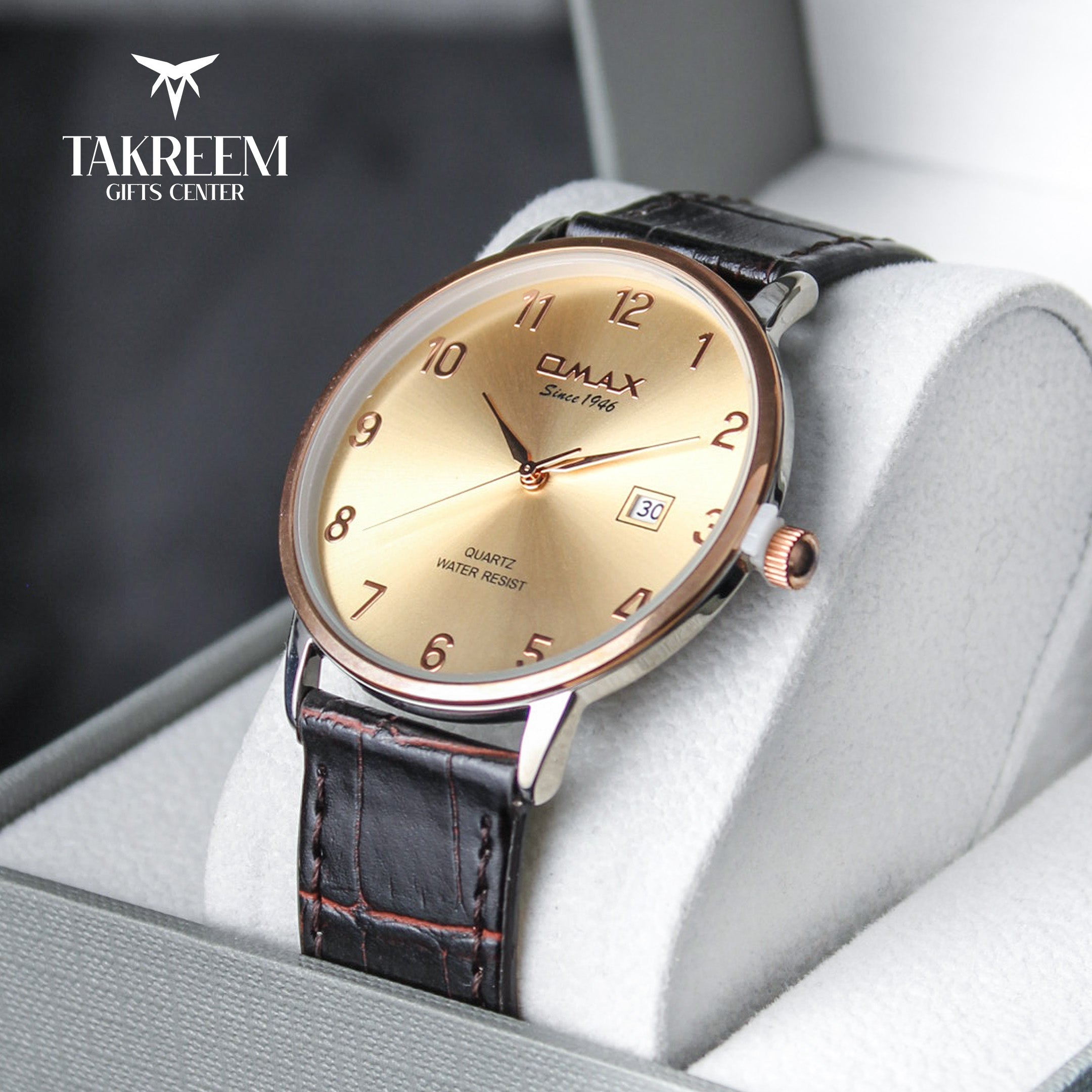 Gold watch with black leather strap on a white cushion, branded 'Takreem Gifts Center'.