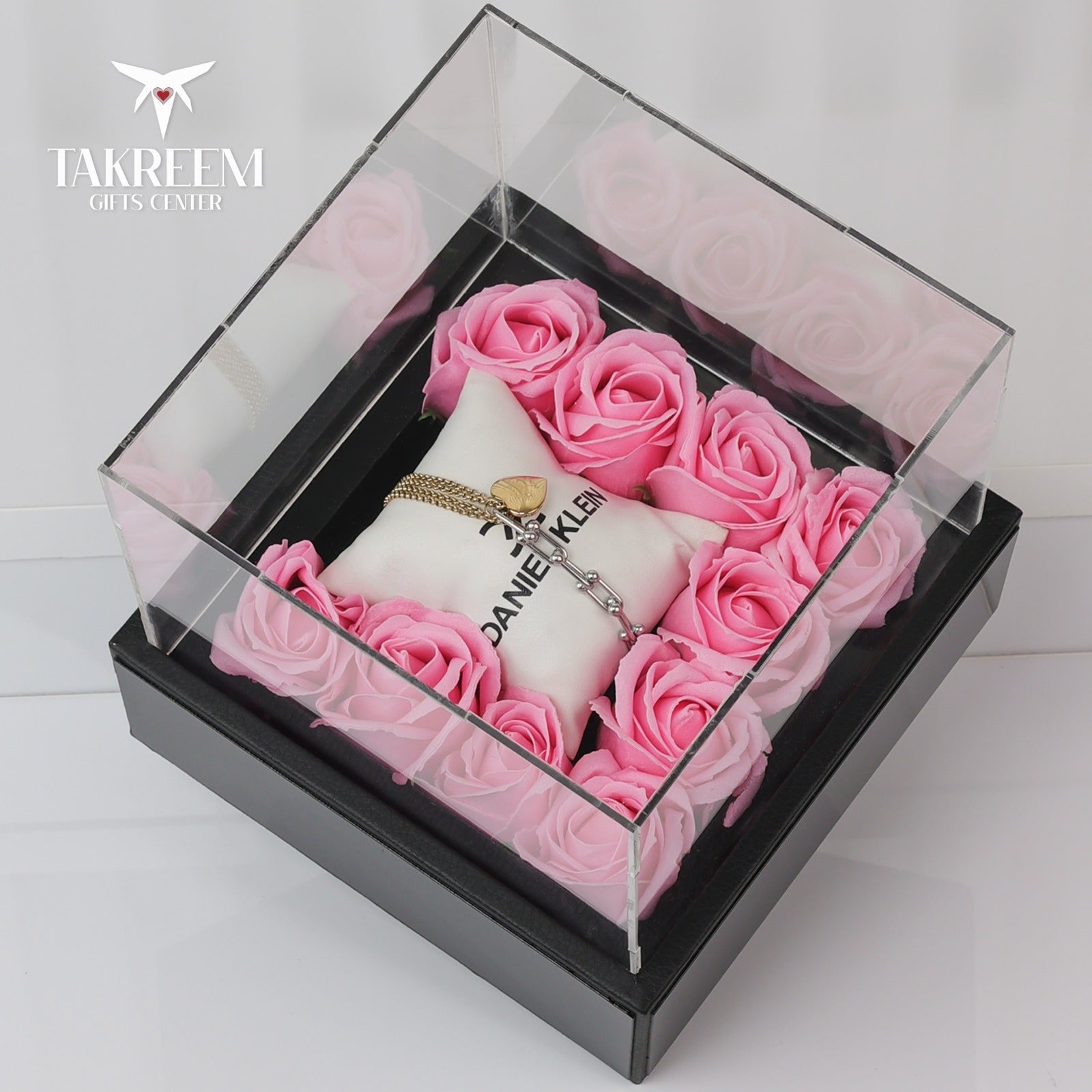 White handbag with pink roses and a necklace in a clear box, branded 'Takreem Gifts Center'.