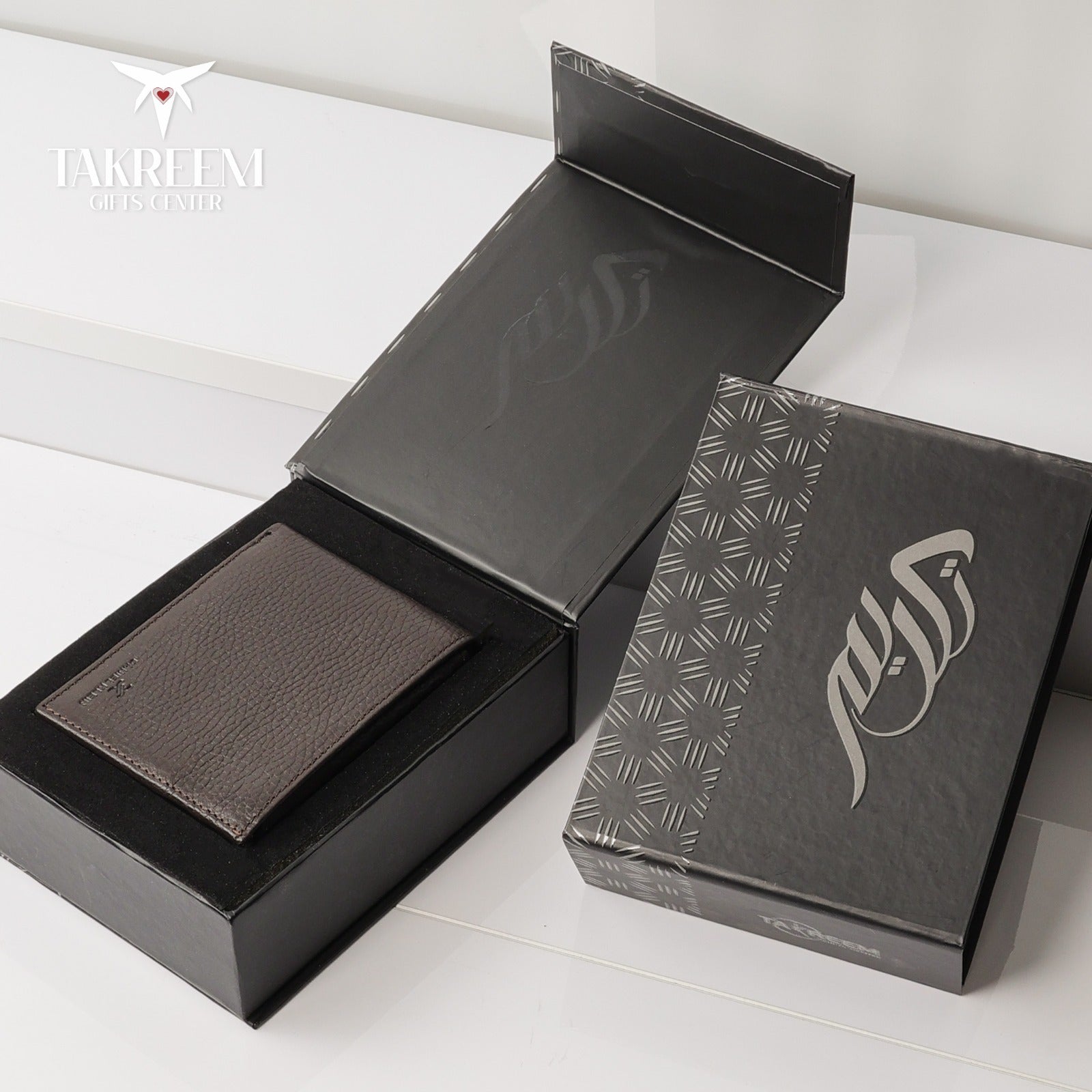 Brown leather wallet in an open black box with a branded box on a white surface