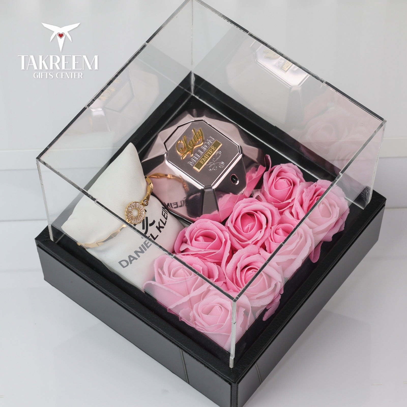Glass display box with pink roses, perfume bottle, and jewelry on a white background