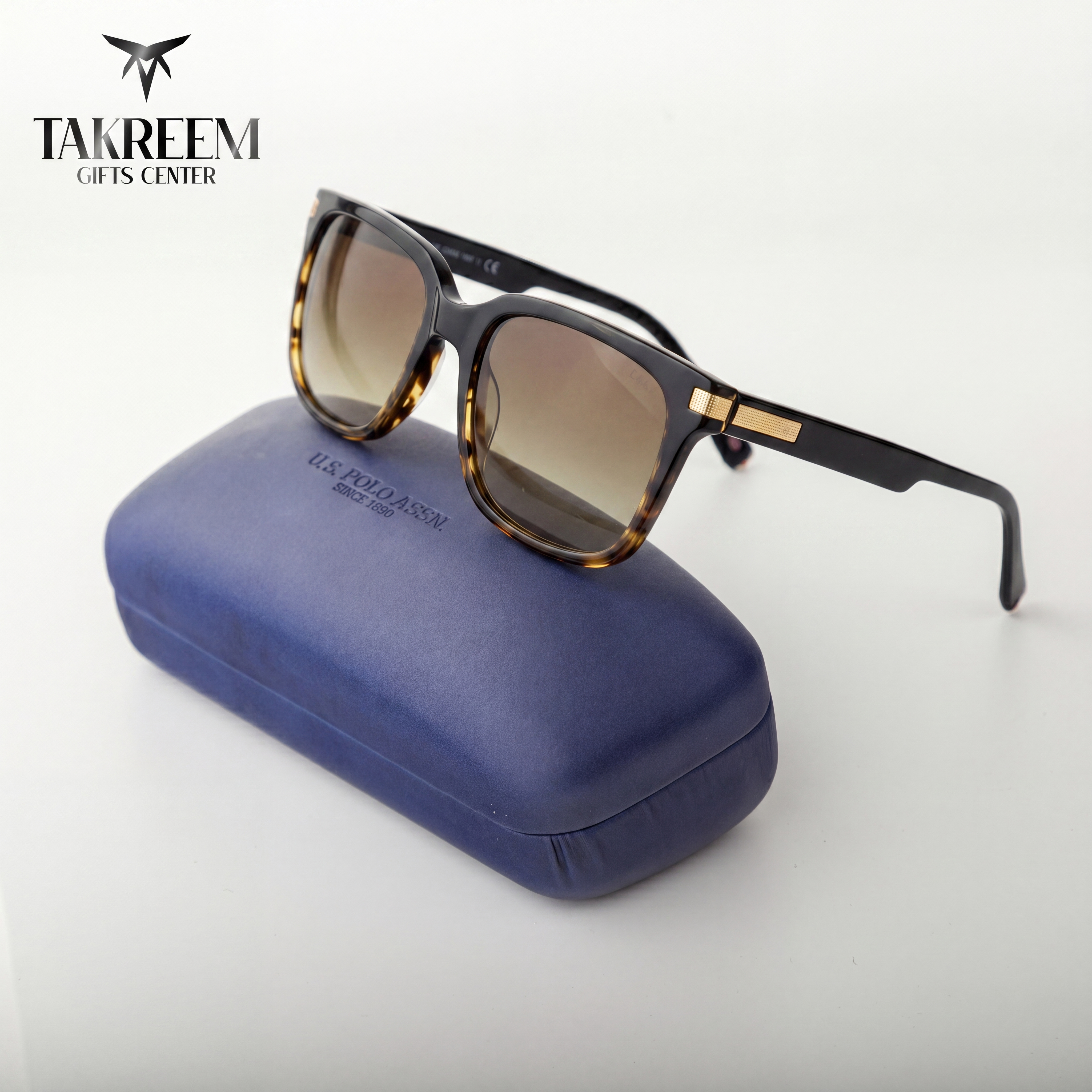 Sunglasses with tortoiseshell frame and brown lenses on a blue case, branded 'Takreem Gifts Center'.