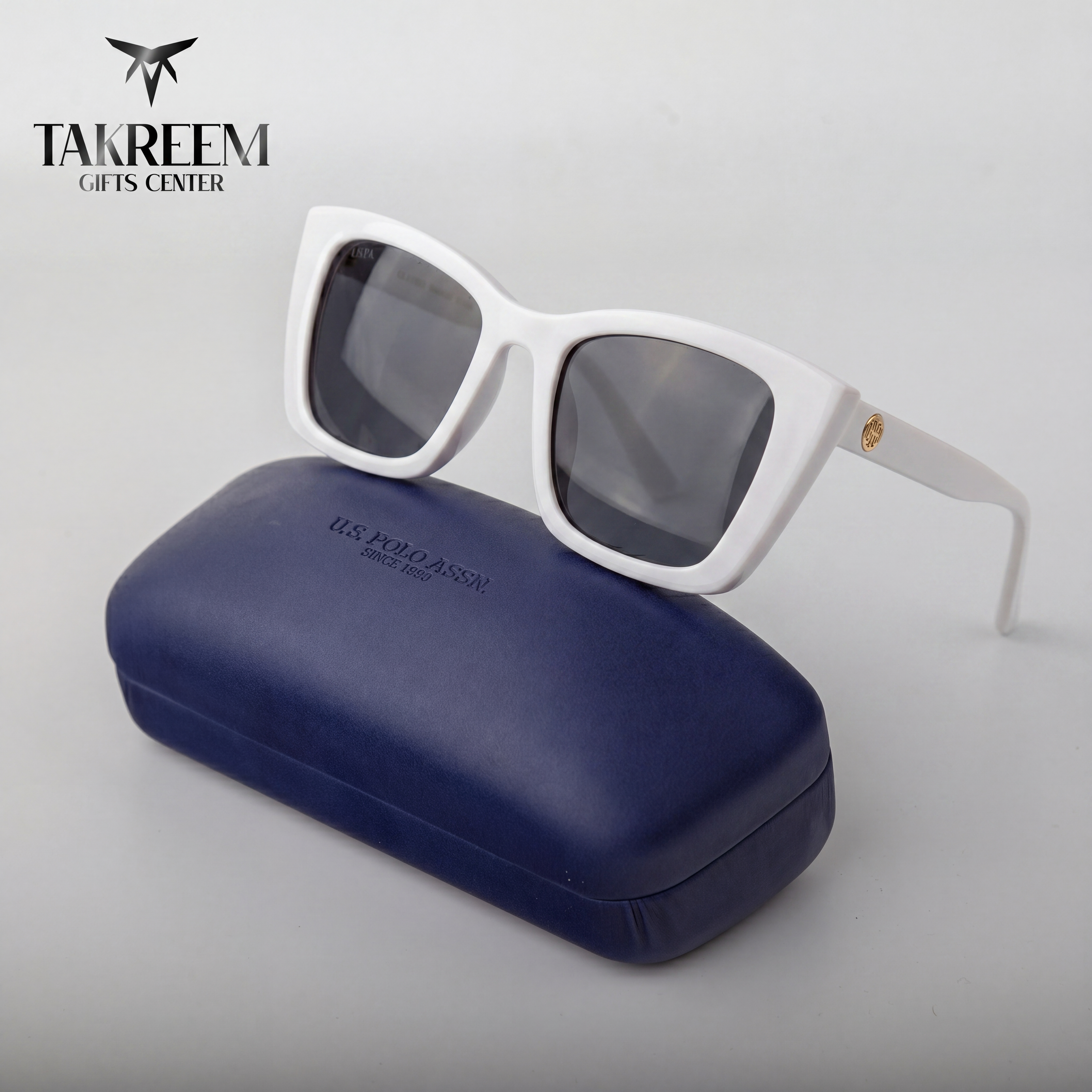 White sunglasses with dark lenses on a blue case, branded 'Takreem Gifts Center'.