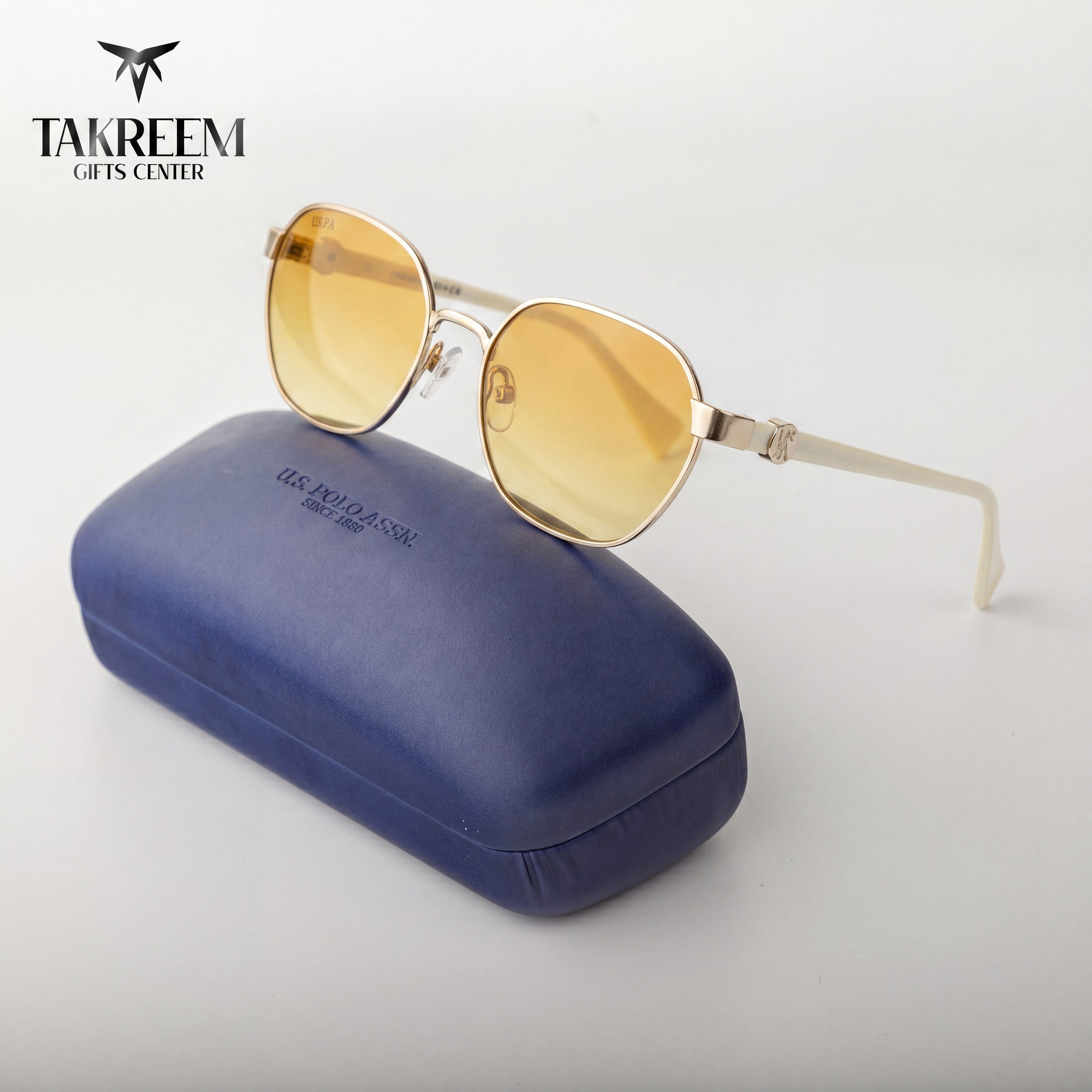 Gold sunglasses with yellow lenses on a blue case, branded 'Takreem Gifts Center'.