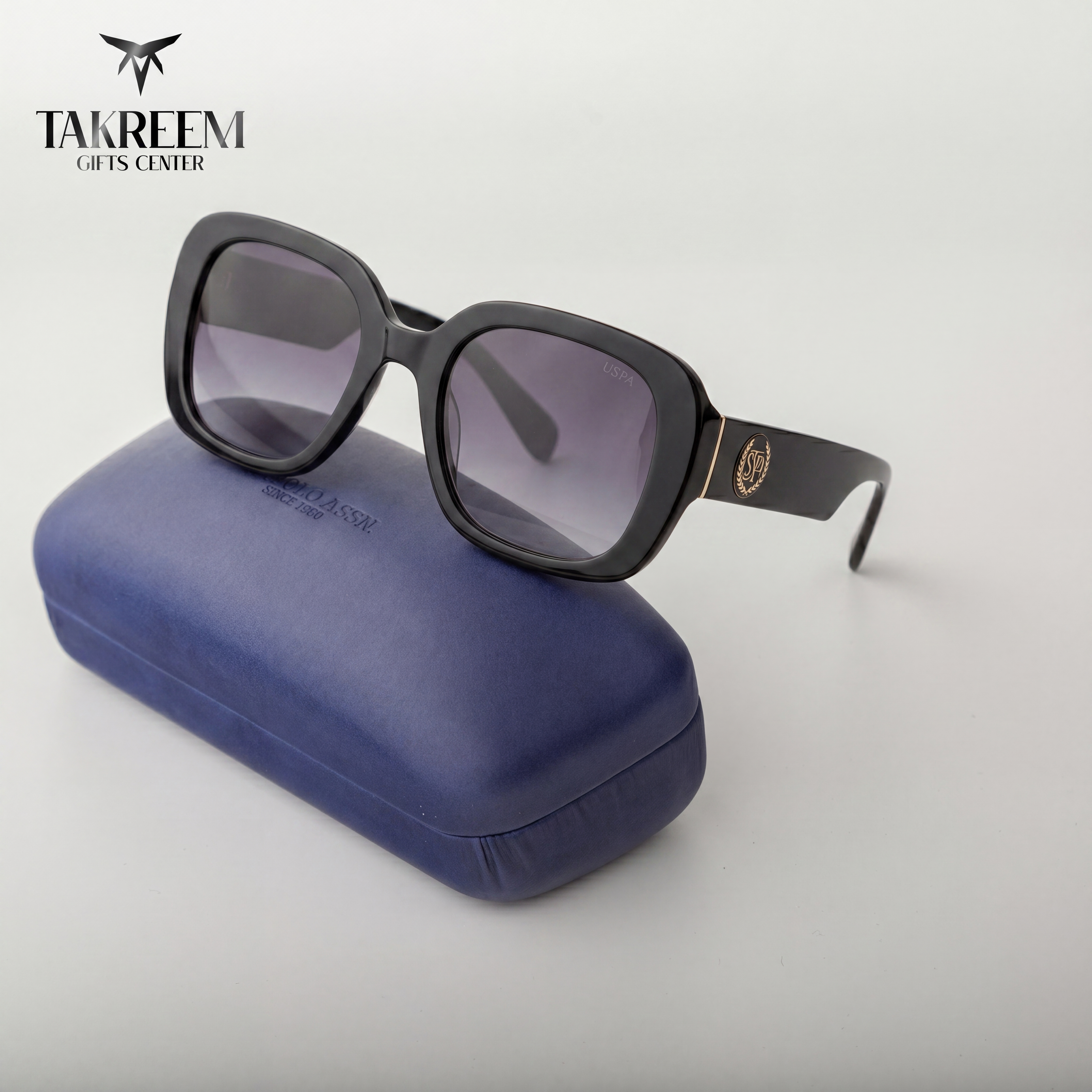 Black sunglasses with a blue case on a light gray background, featuring the Takreem Gifts Center logo.