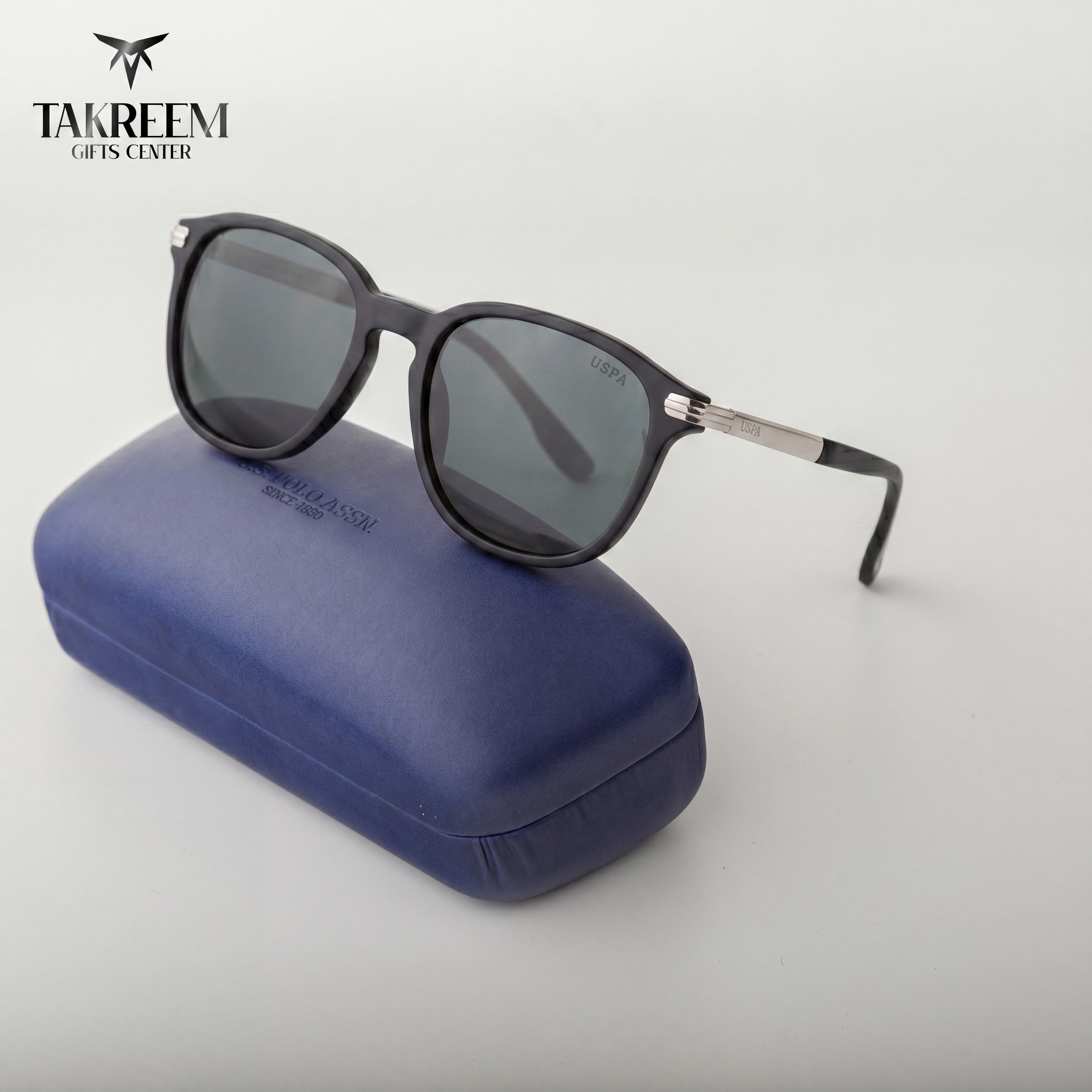 Black sunglasses with dark lenses on a blue case, branded 'Takreem'.
